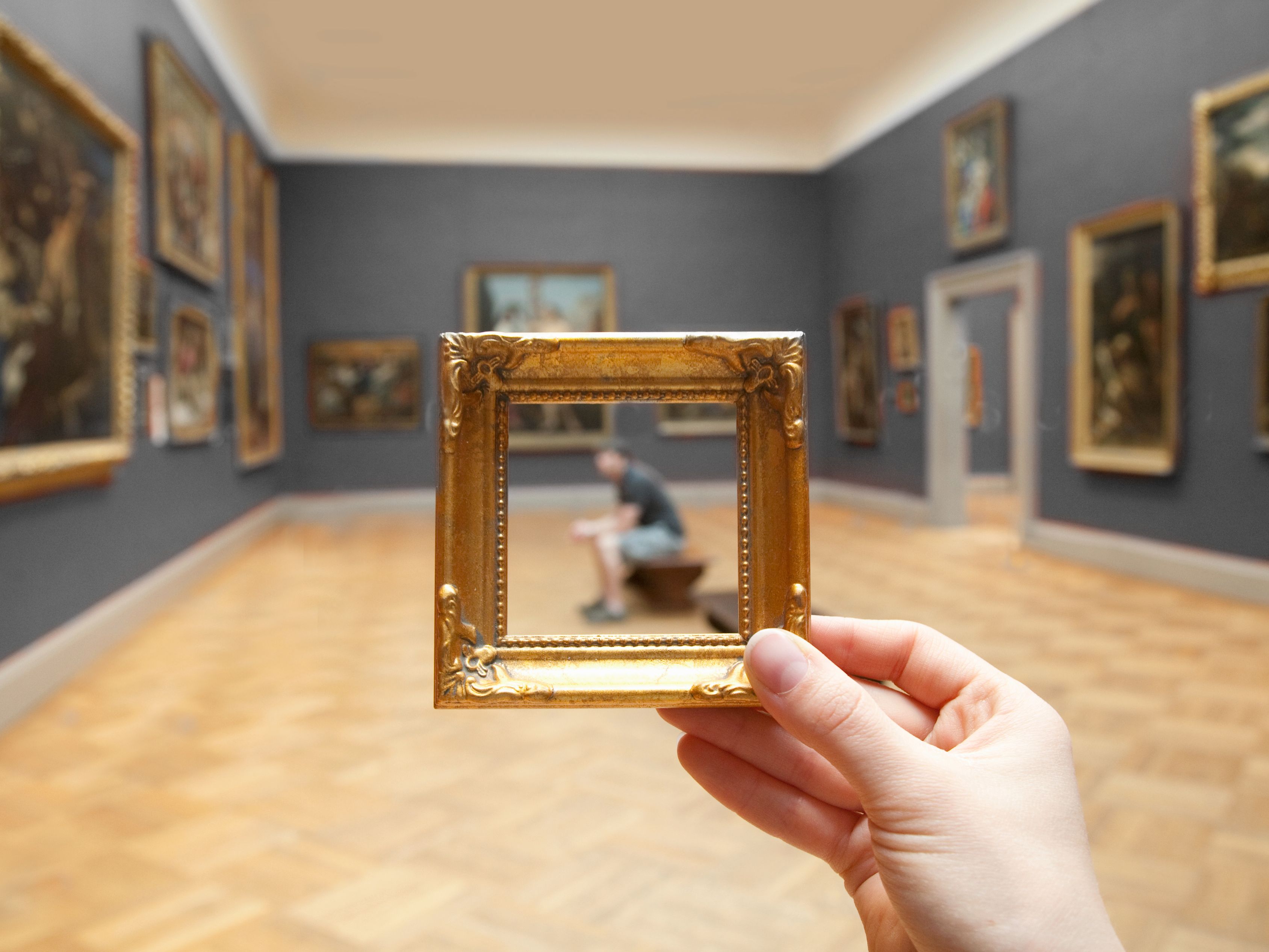 Man sitting in museum being framed by small gold frame by photographer