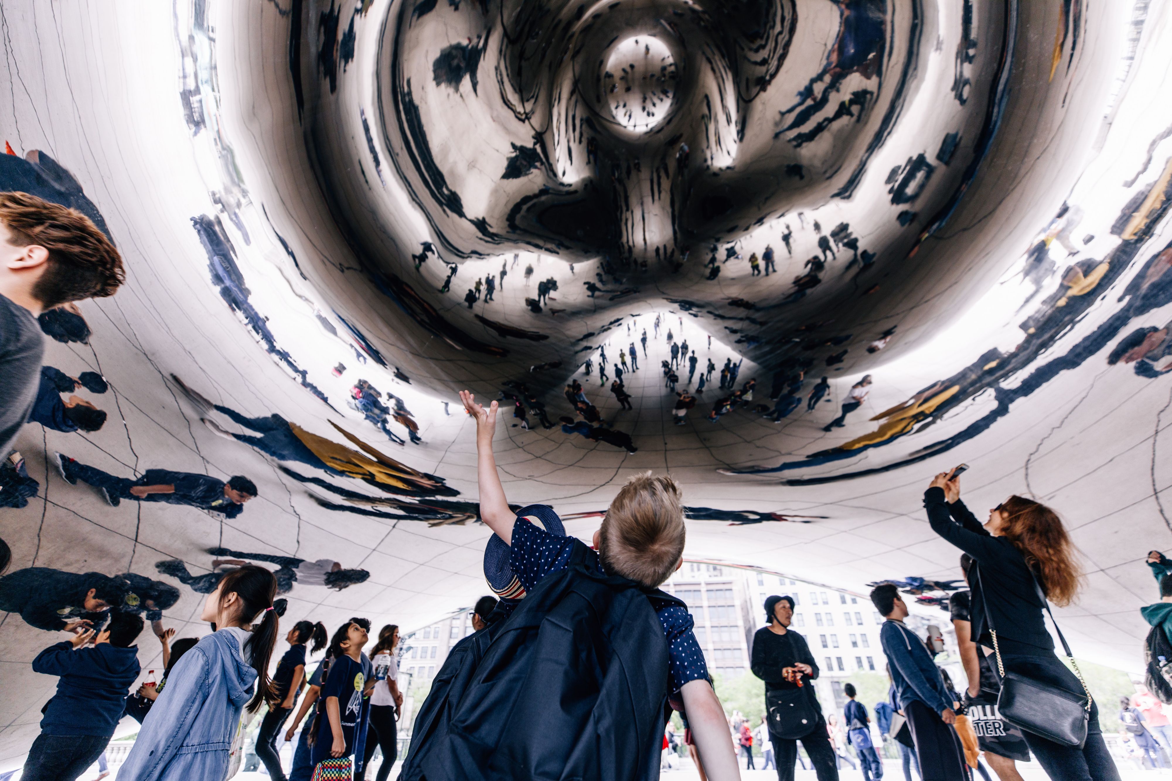Visitors beneath Cloud Gate reflecting Chicago skyline and crowd.