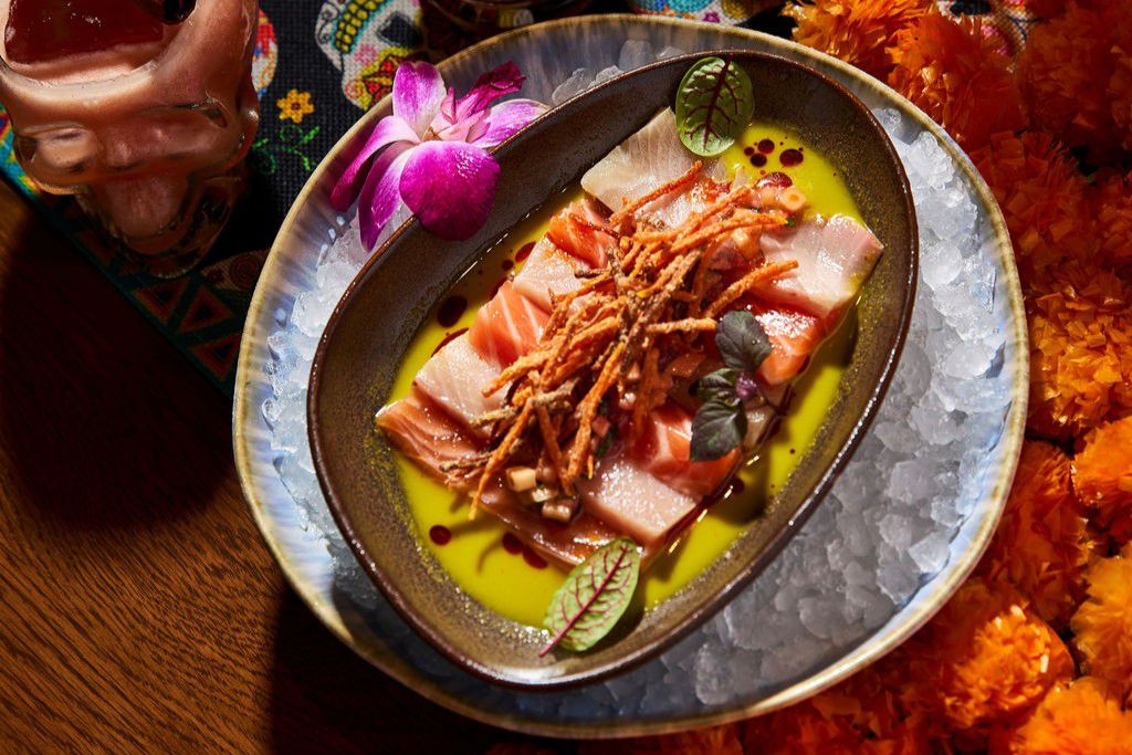 Plated seafood dish with crispy garnish, sauce, and edible flowers
