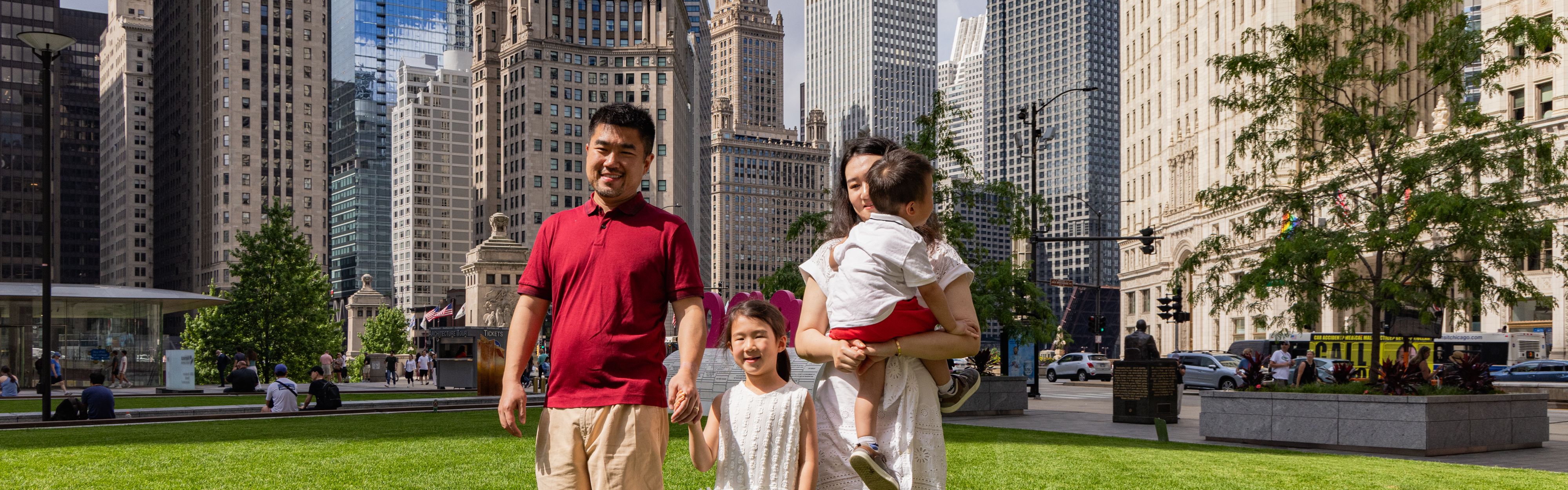 Family walking through a downtown park surrounded by skyscrapers.