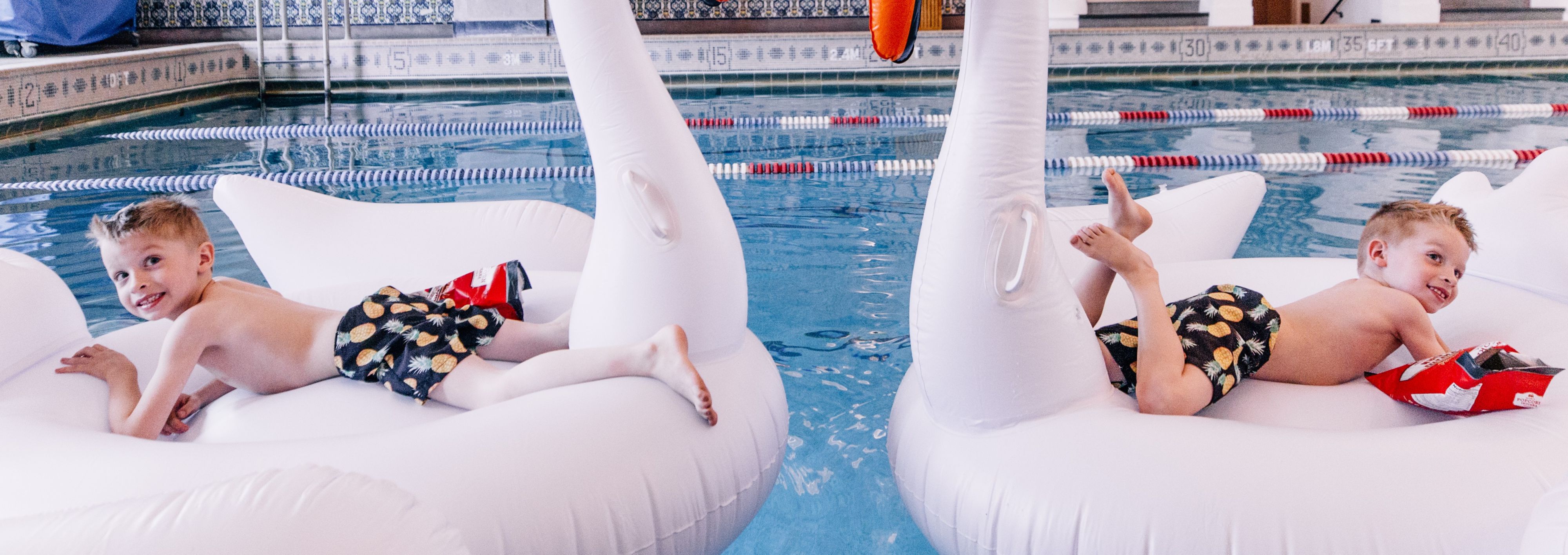 Two kids on swan floaties in pool