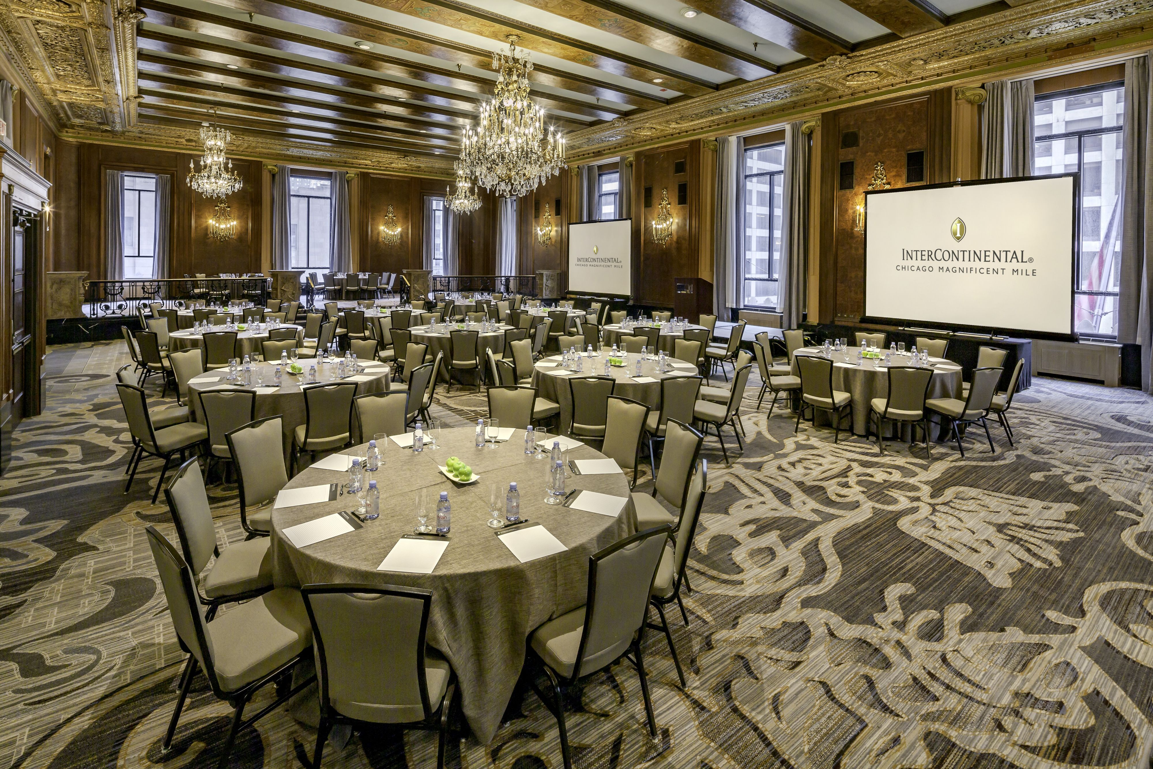 Elegant ballroom meeting space with round tables, chandeliers, and presentation screens.