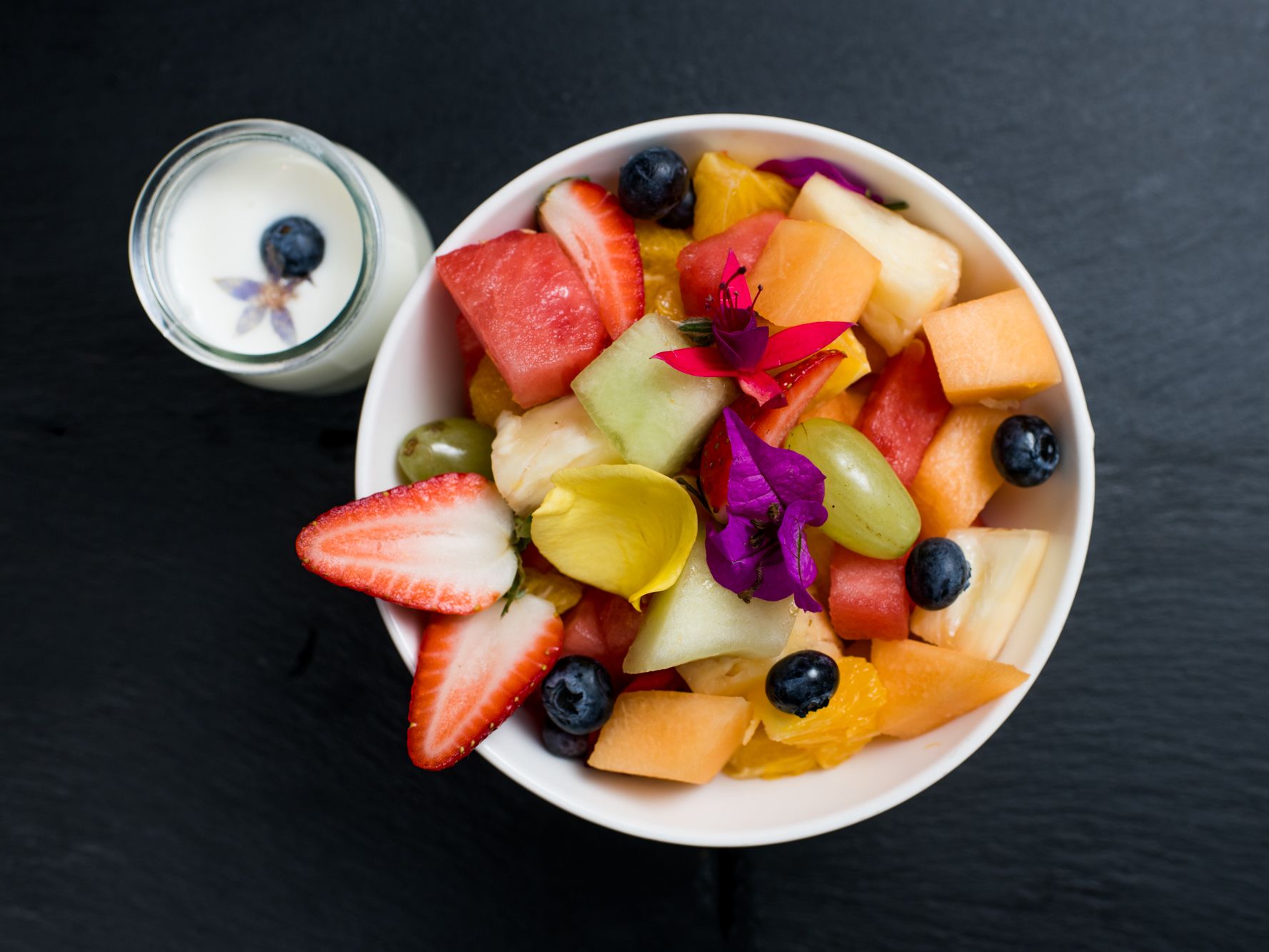 Fruit bowl with a side of blueberry-garnished milk.