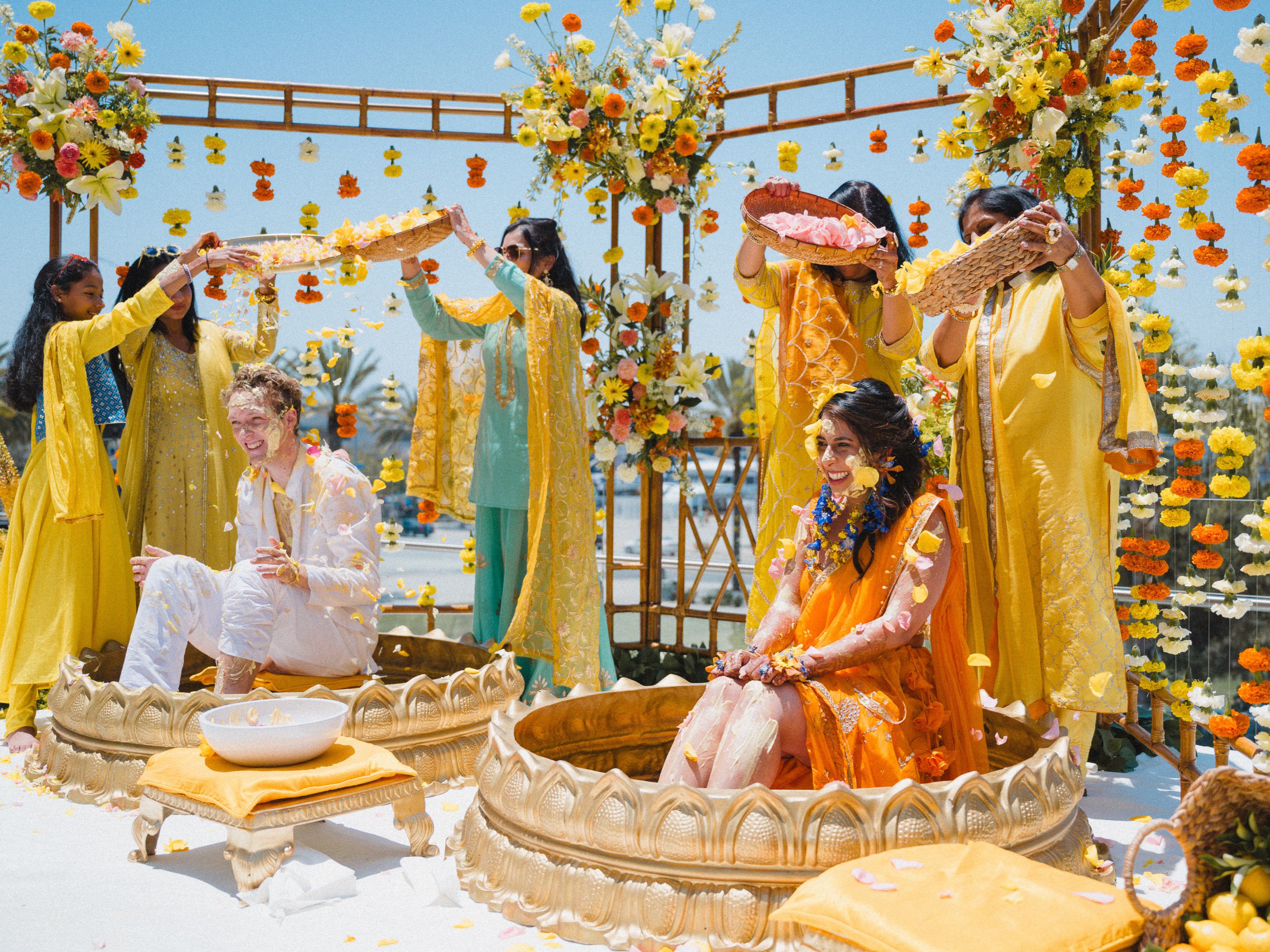 Outdoor celebration with floral garlands, marigold decorations, and guests gathered by the waterfront.