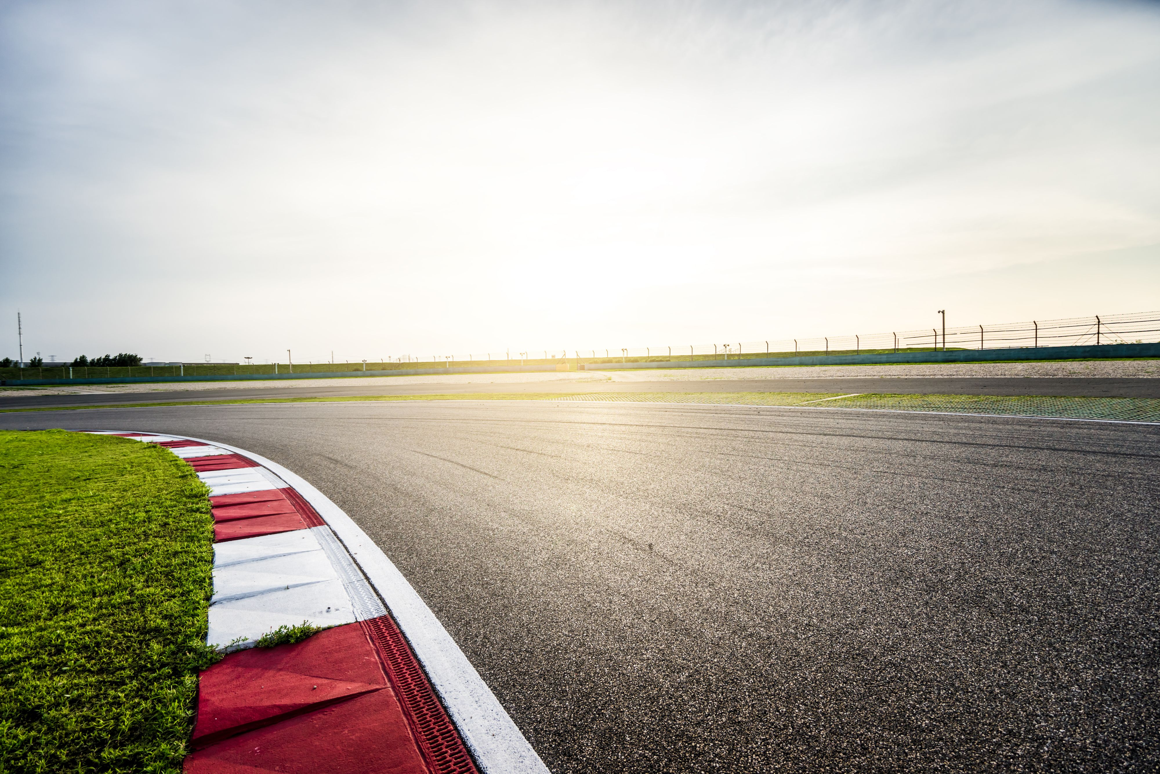 Wide view of a racetrack curve at sunset, featuring red and white curbs and open grassy infield.