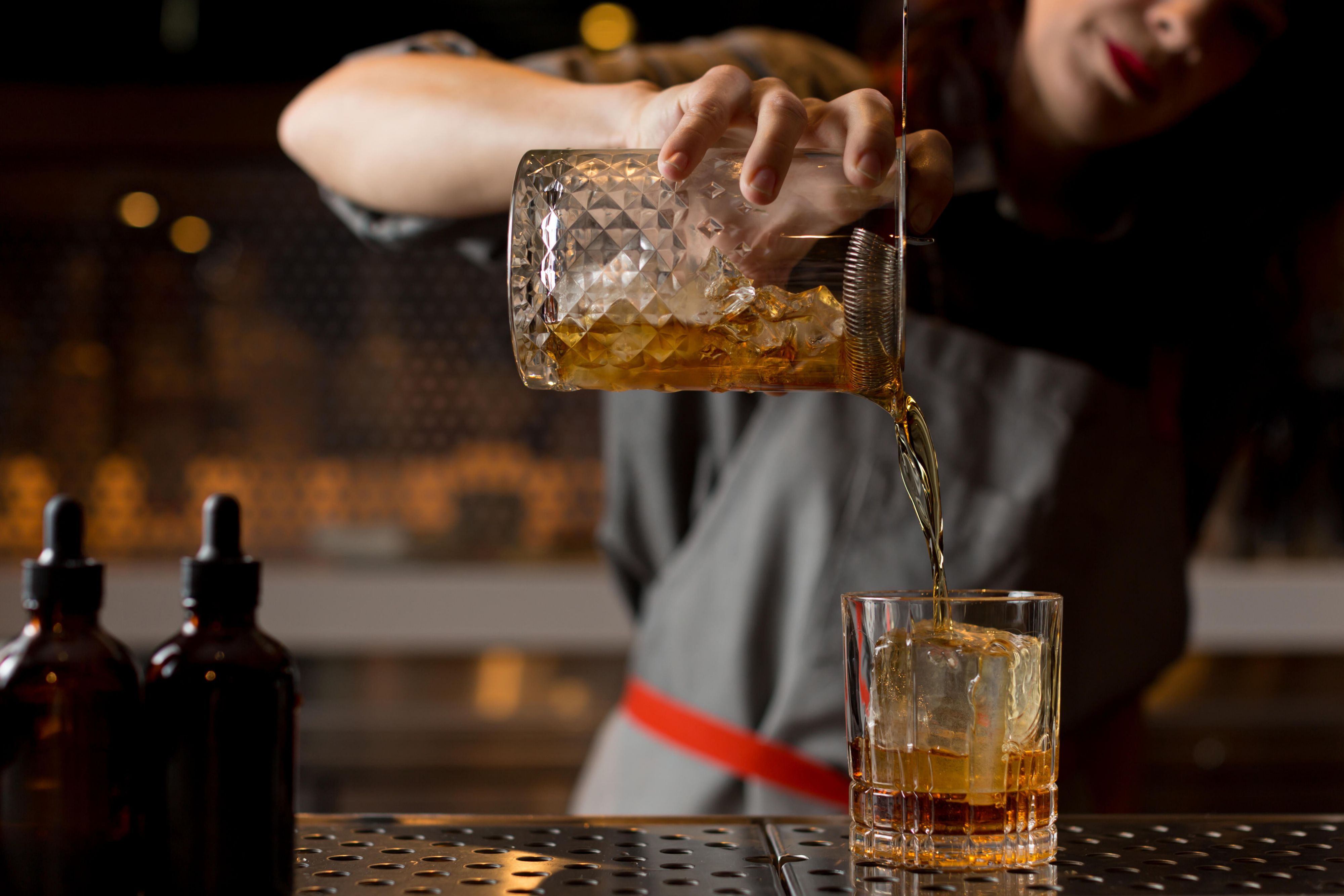 Bartender pouring an amber cocktail over ice in a glass.