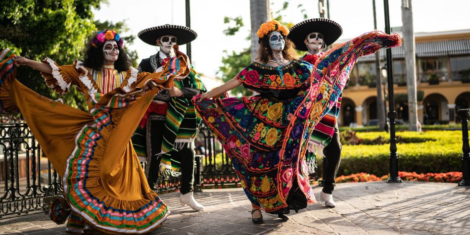 Performers in traditional dress and skull makeup dancing outdoors.
