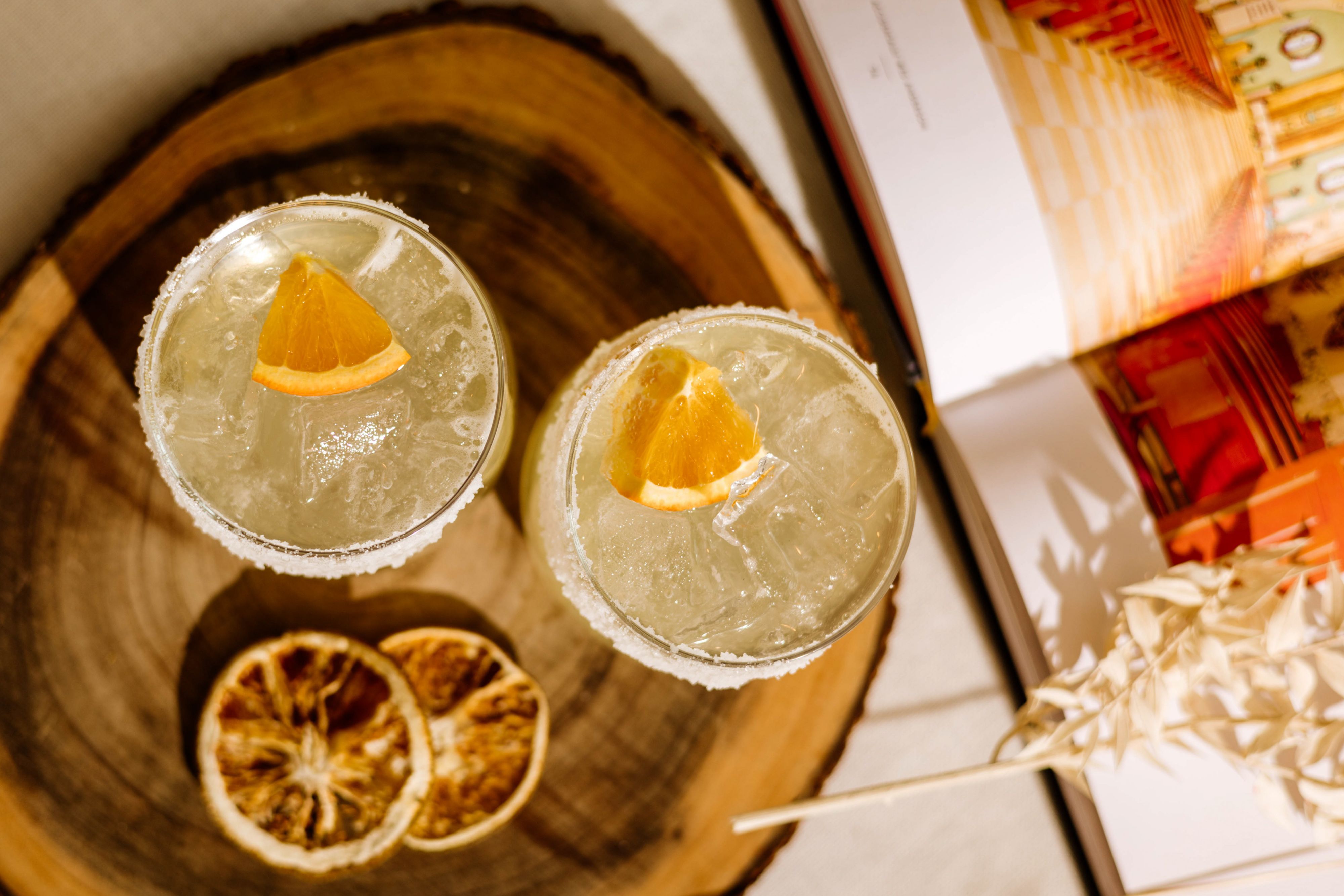Two craft cocktails garnished with dried citrus on a serving tray