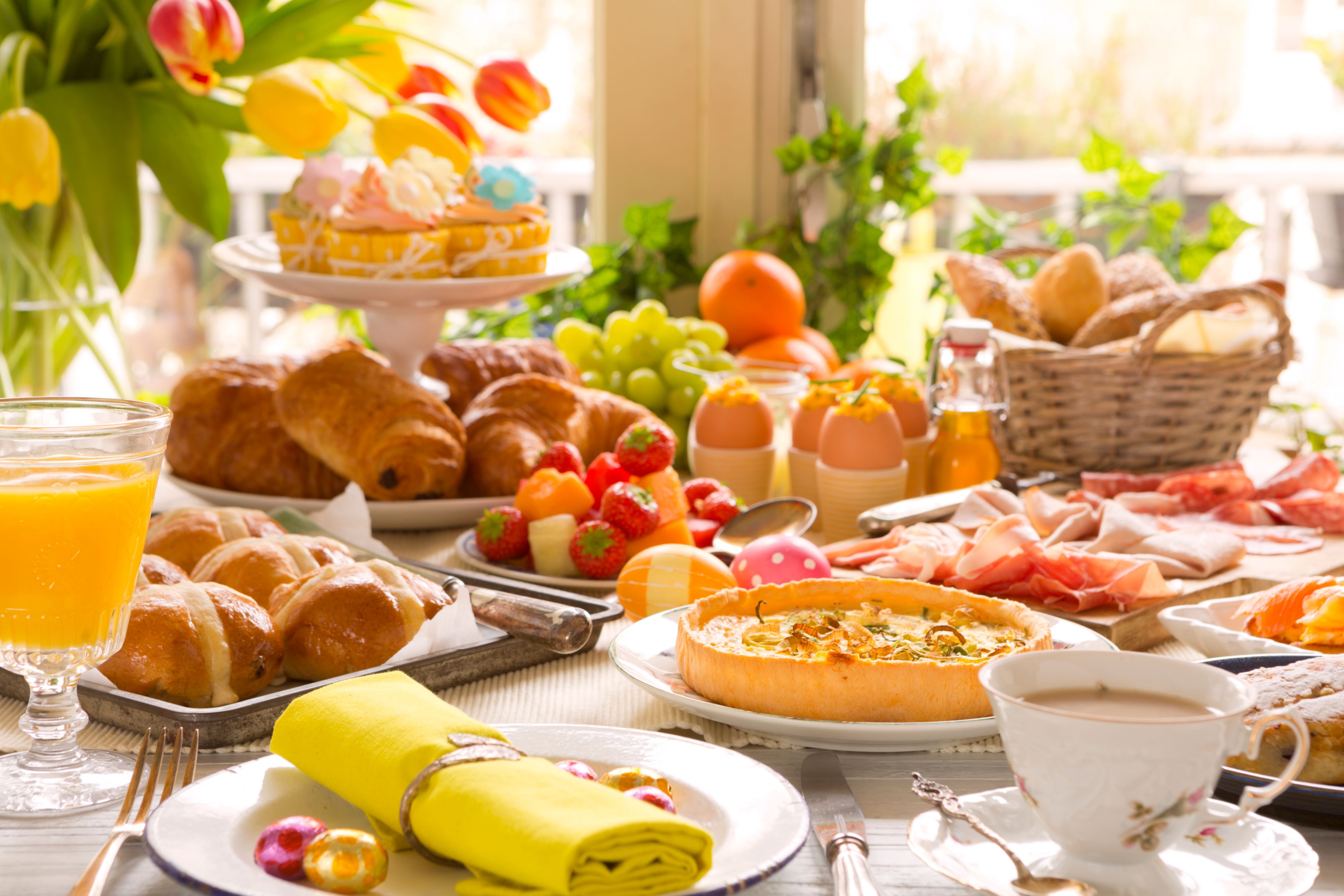 Colorful spring brunch table with pastries, fruit, quiche, and drinks.
