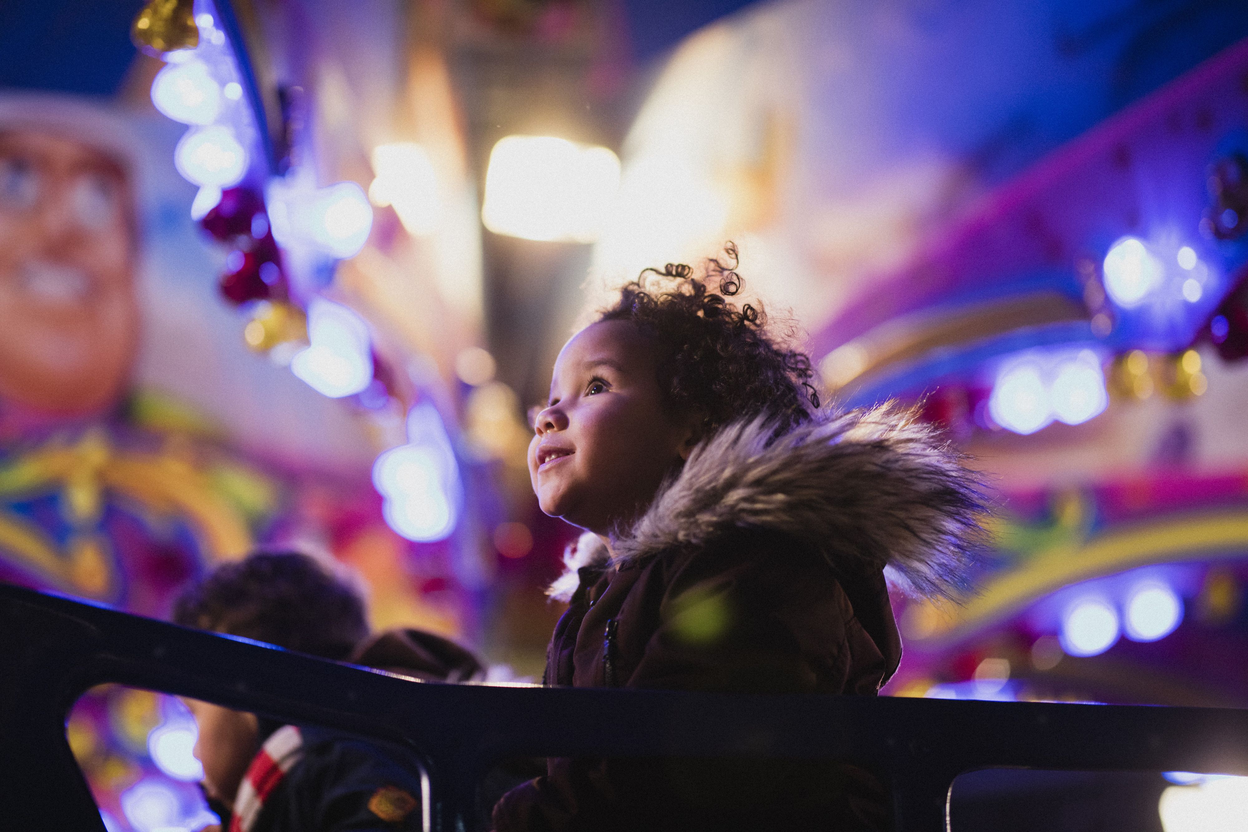 Child in a fur-trimmed coat surrounded by colorful lights
