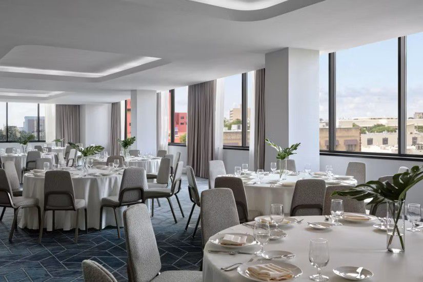 Spacious event room with round banquet tables, large windows, and city views.