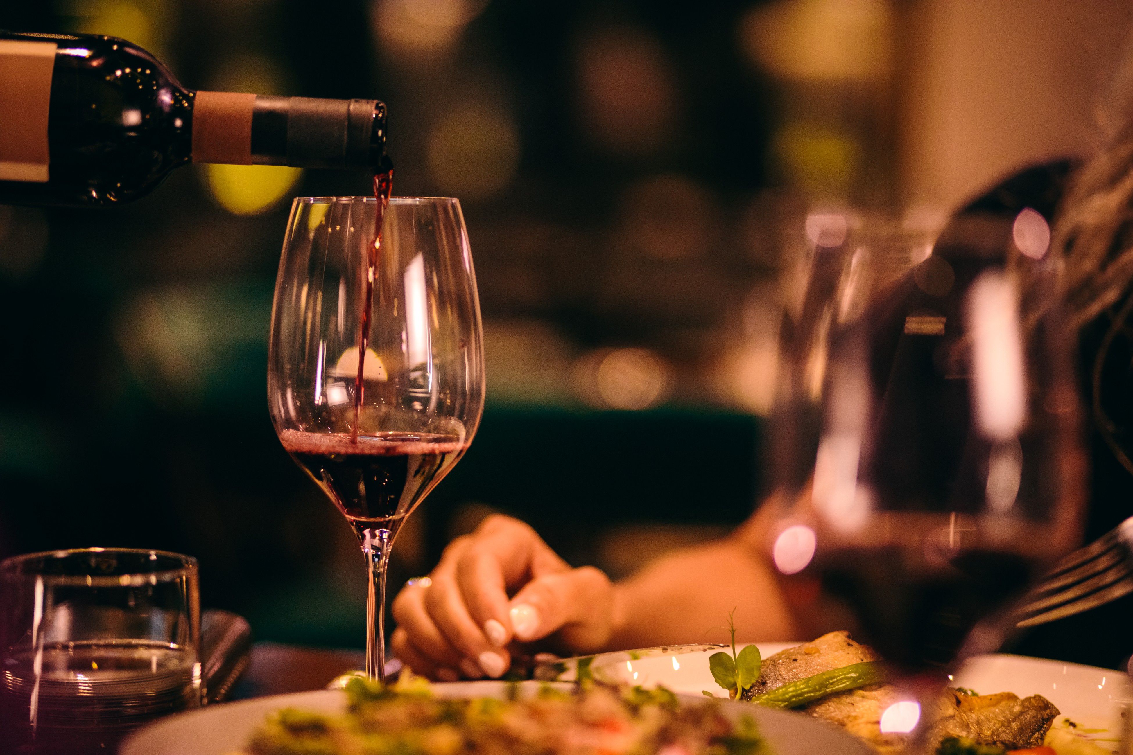 Red wine being poured into a glass during a restaurant dining experience.