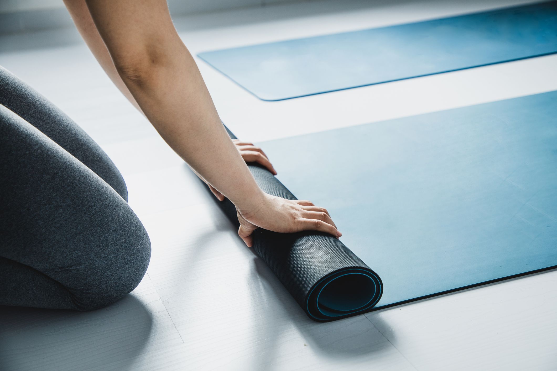 Hands unrolling a yoga mat in preparation for a wellness session.