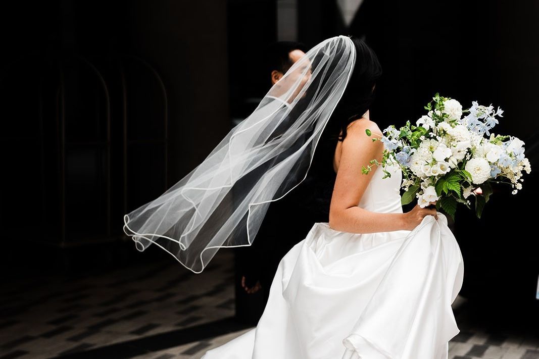 Wedding portrait featuring a flowing veil, white floral bouquet, and elegant gown in a modern indoor venue setting.