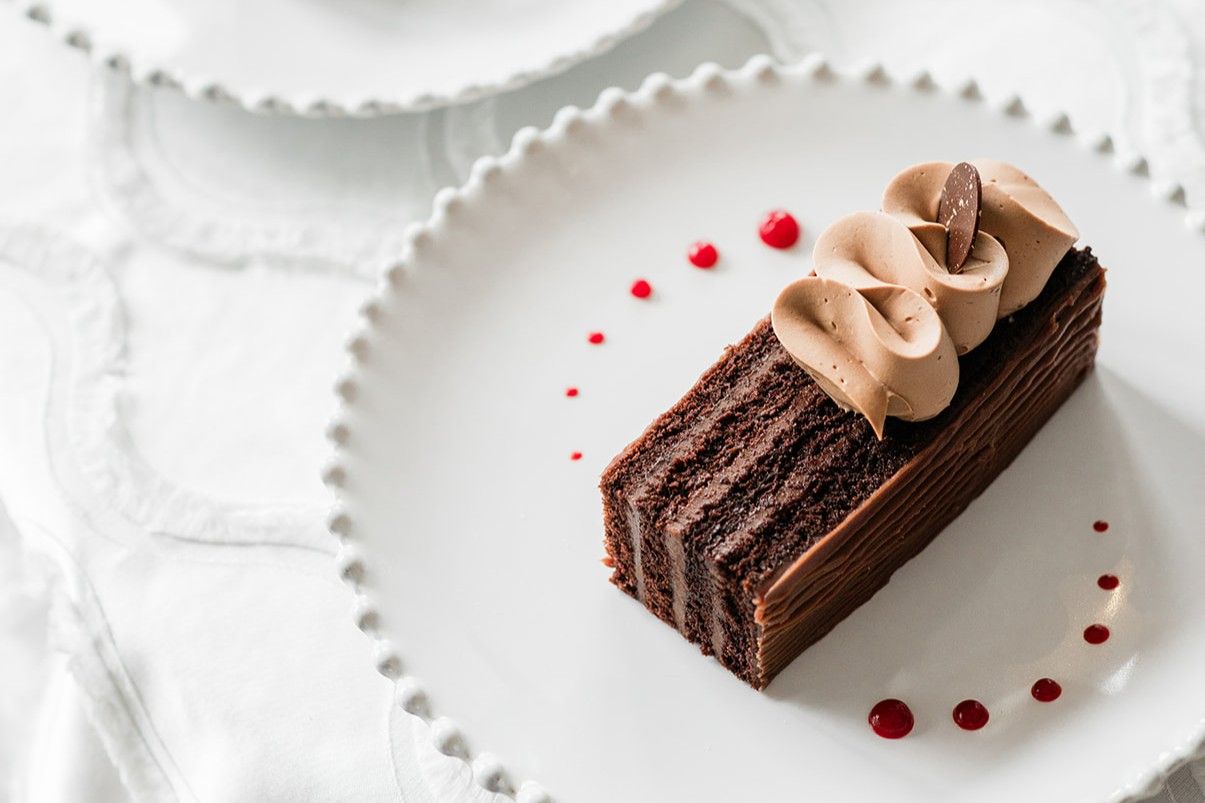 Plated chocolate cake with piped frosting and berry sauce accents served on a decorative white dessert plate.