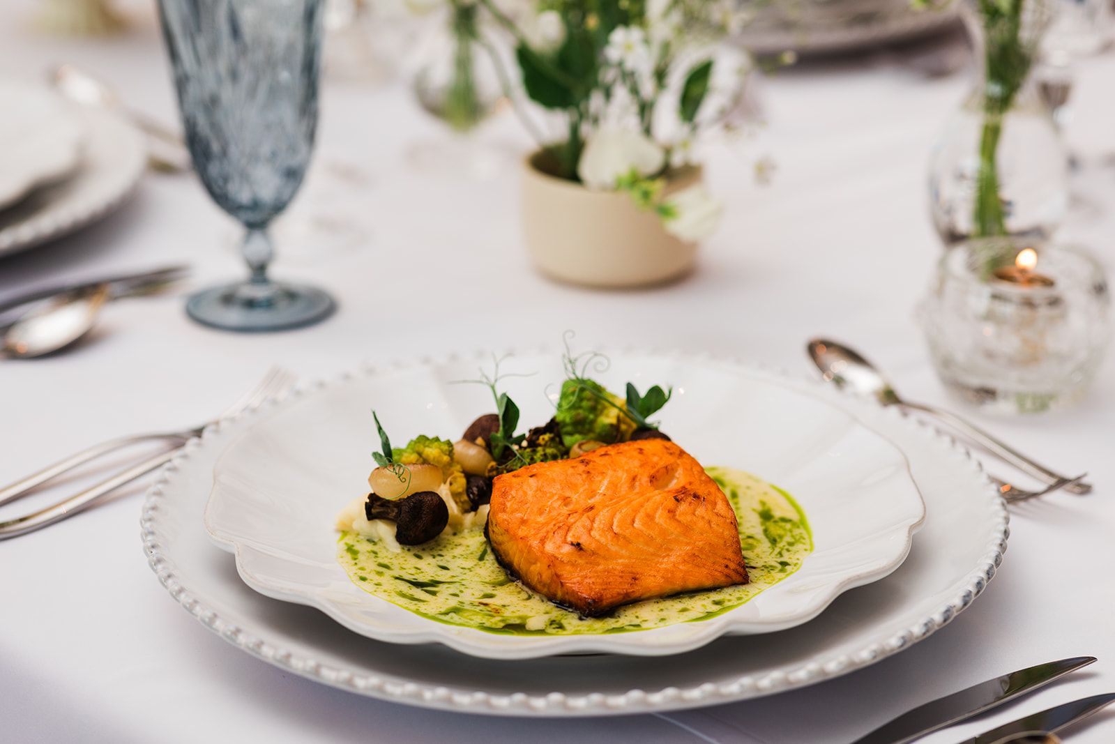 Grilled salmon fillet served with seasonal vegetables and herb sauce on an elegant white plate set for a formal wedding reception meal.
