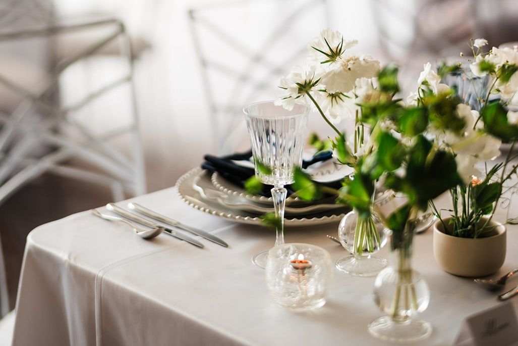 Elegant wedding reception table with white floral arrangements, crystal glassware, candlelight, and refined place settings with navy napkins.