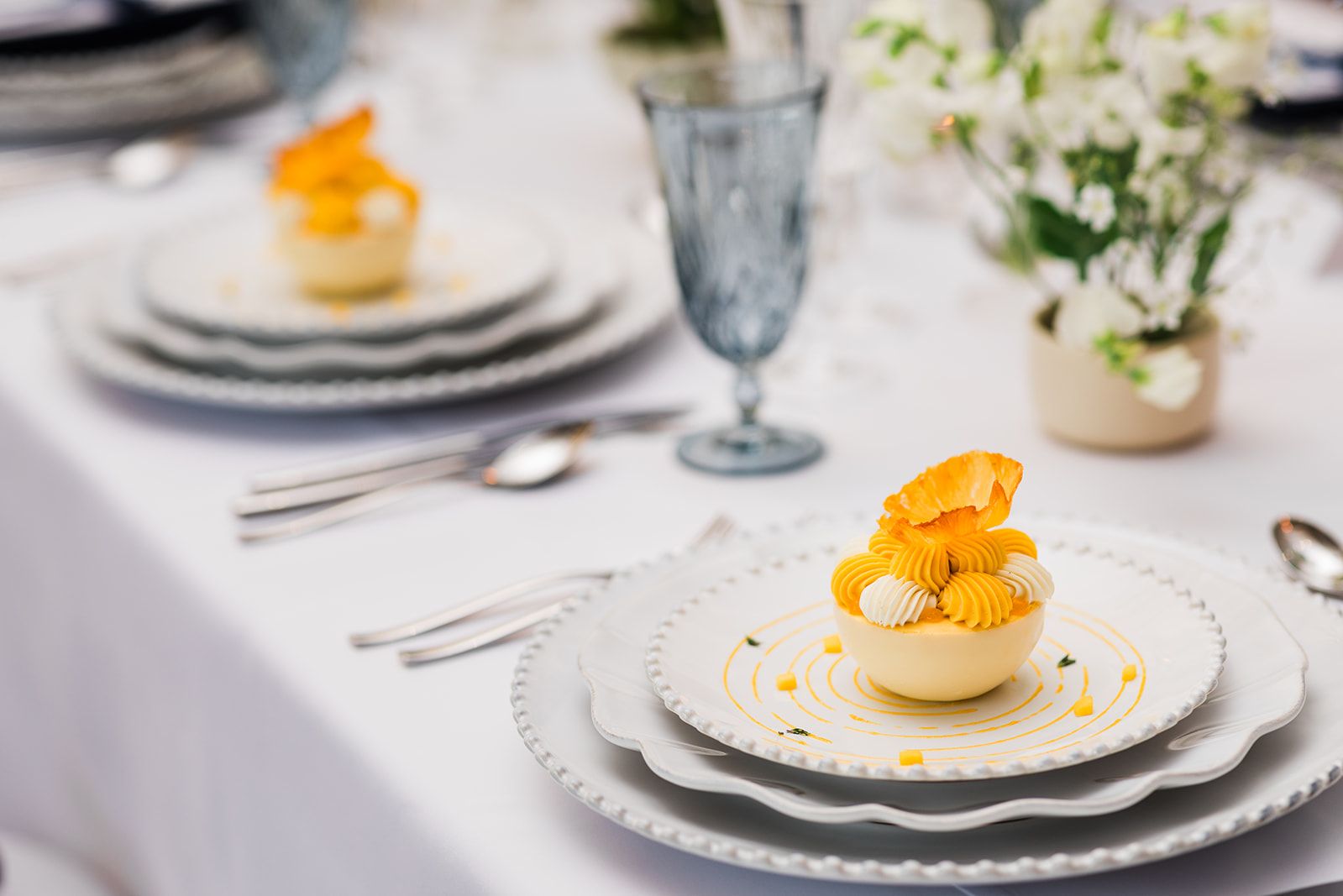 Elegant plated dessert with citrus garnish served on fine china at a wedding reception table adorned with crystal glassware and white floral arrangements.