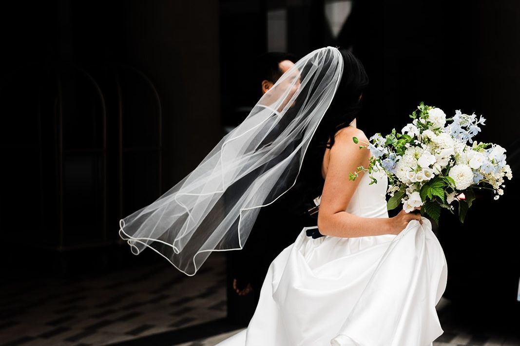 Wedding portrait featuring a flowing veil, white floral bouquet, and elegant gown in a modern indoor venue setting.
