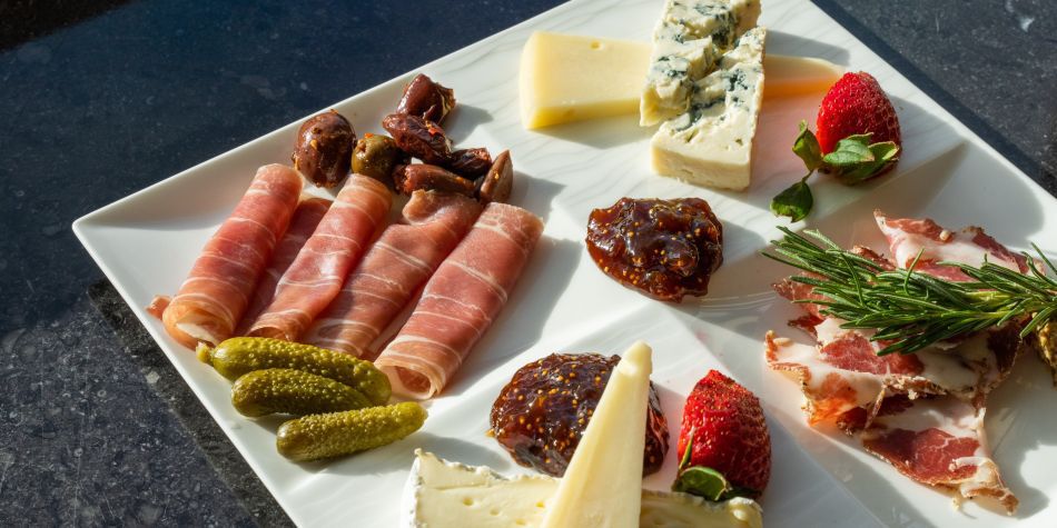 Charcuterie plate with prosciutto, assorted cheeses, pickled vegetables, fig jam, and fresh herbs served at Top of the Mark in San Francisco.
