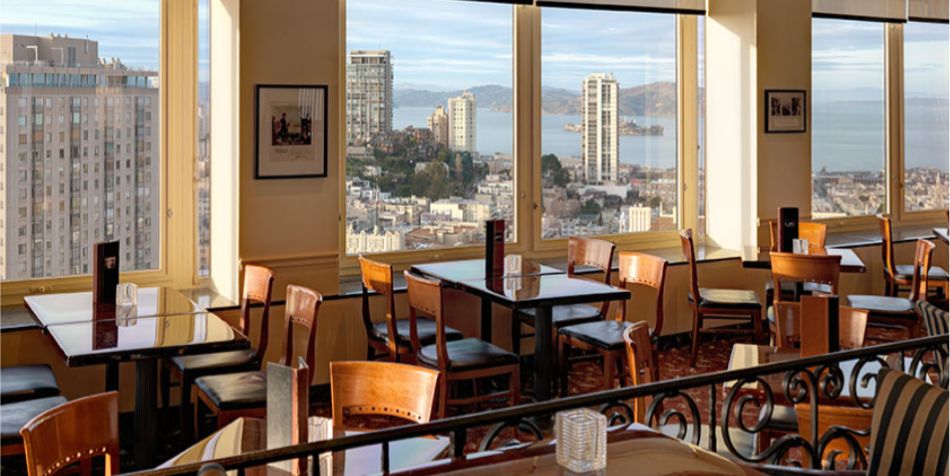 Dining room at Top of the Mark featuring wooden tables, large windows, and panoramic city and bay views.
