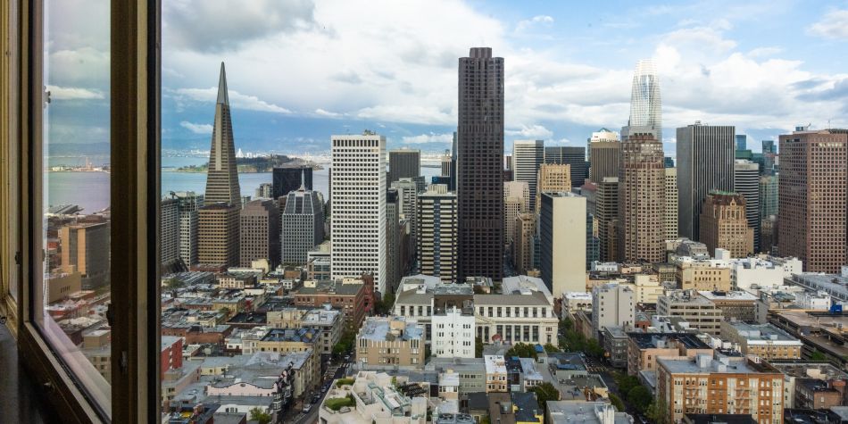 View of the San Francisco skyline from a window, featuring downtown skyscrapers and the Transamerica Pyramid under a partly cloudy sky.