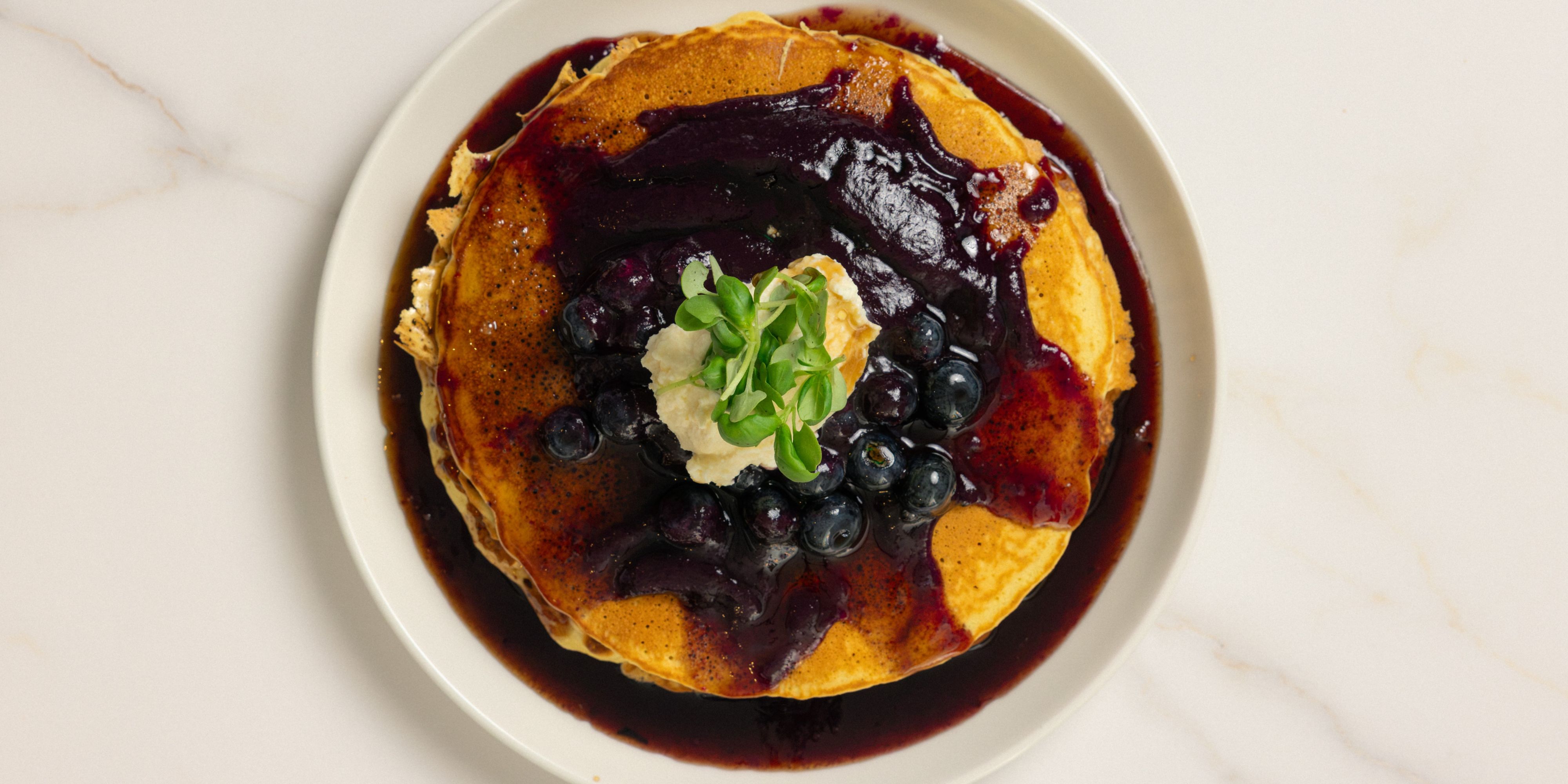 Stack of pancakes topped with blueberry compote and whipped cream