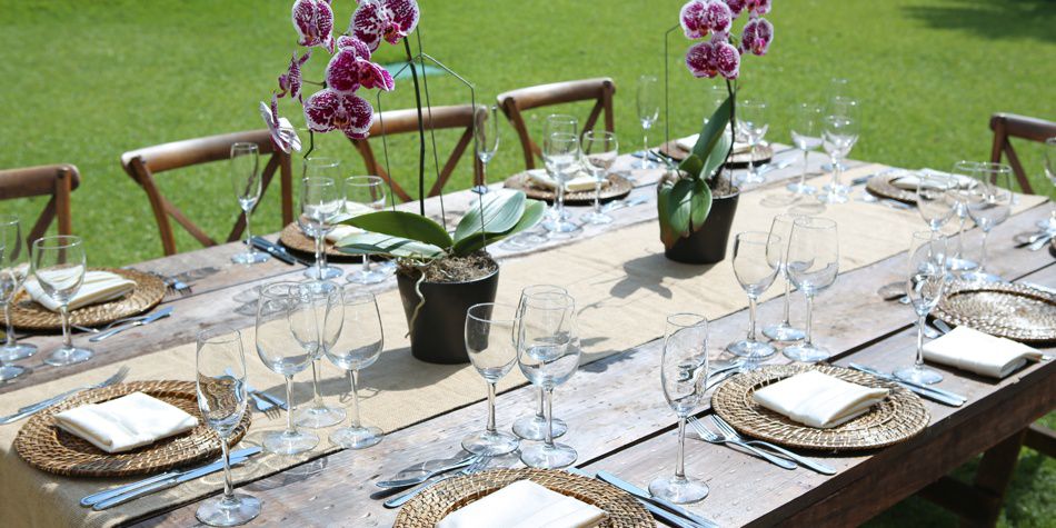 Mesa de comedor al aire libre con orquídeas, cubiertos y cristalería