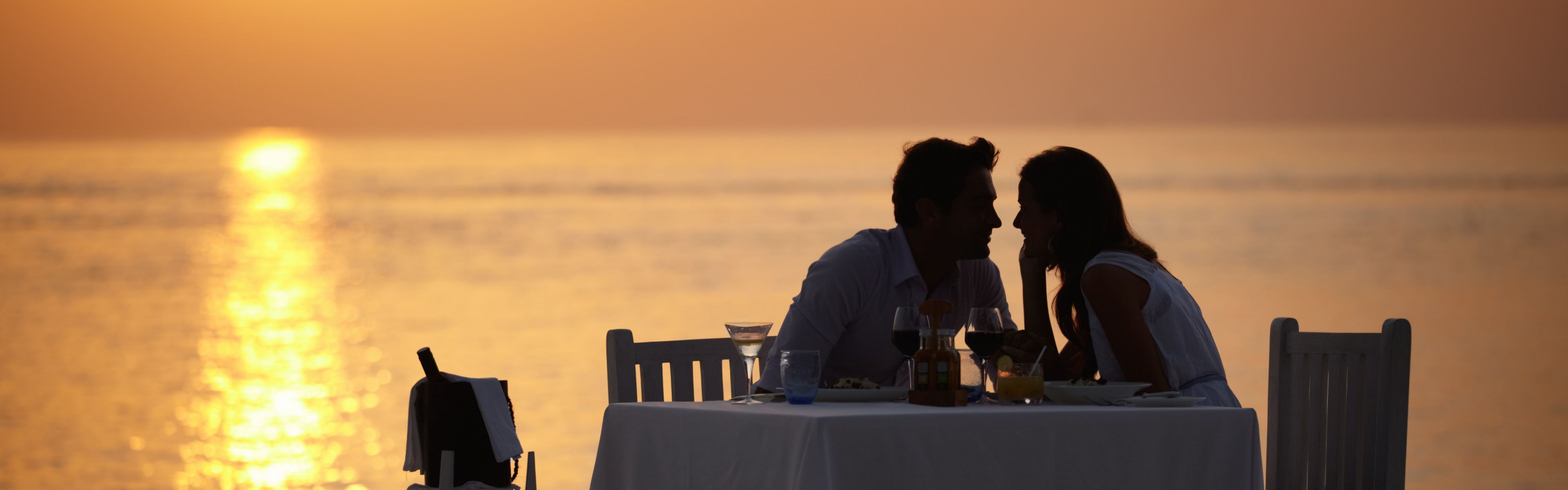 Two people dining by the water at sunset.