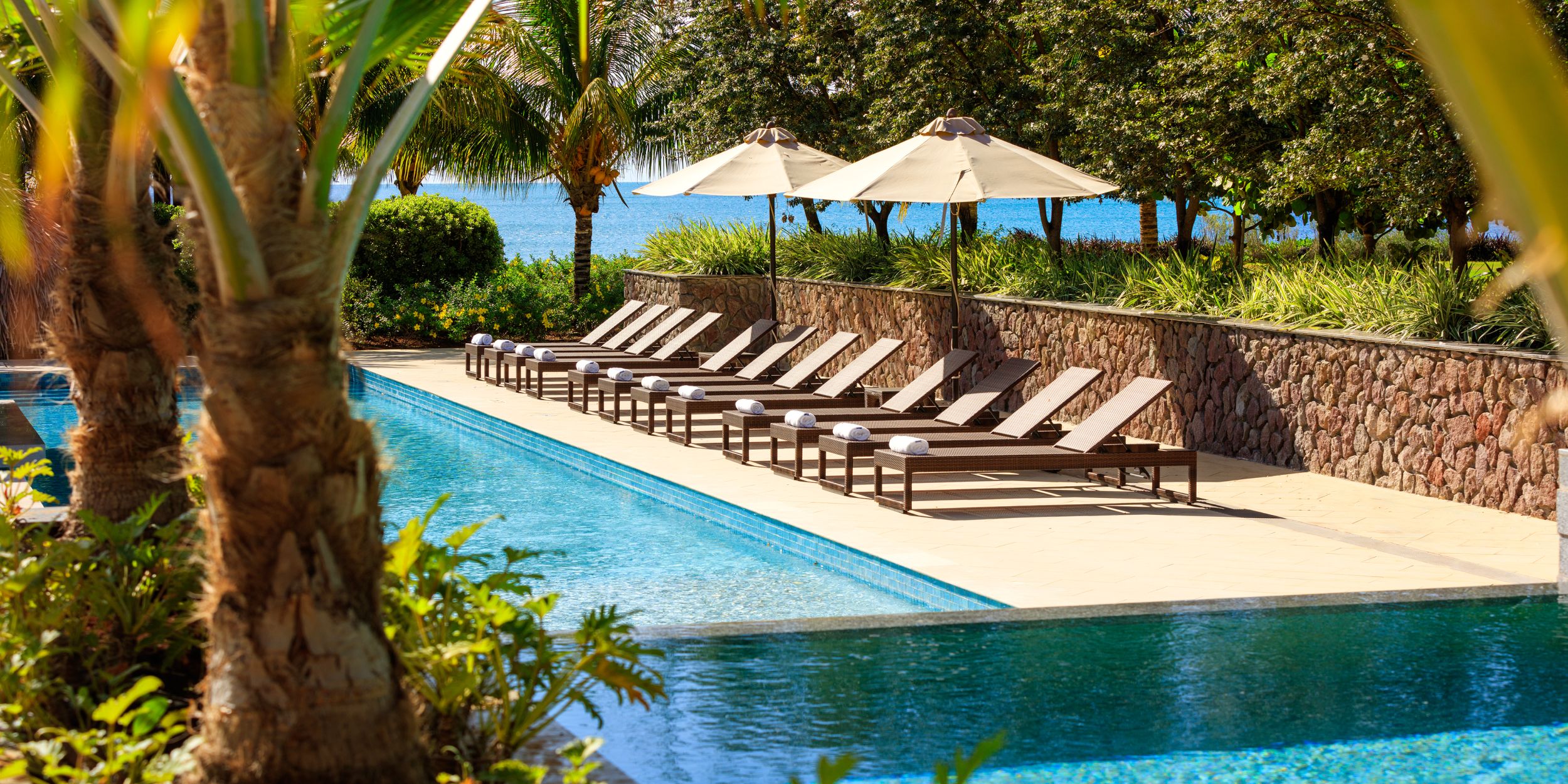 A swimming pool with lounge chairs near a body of water.