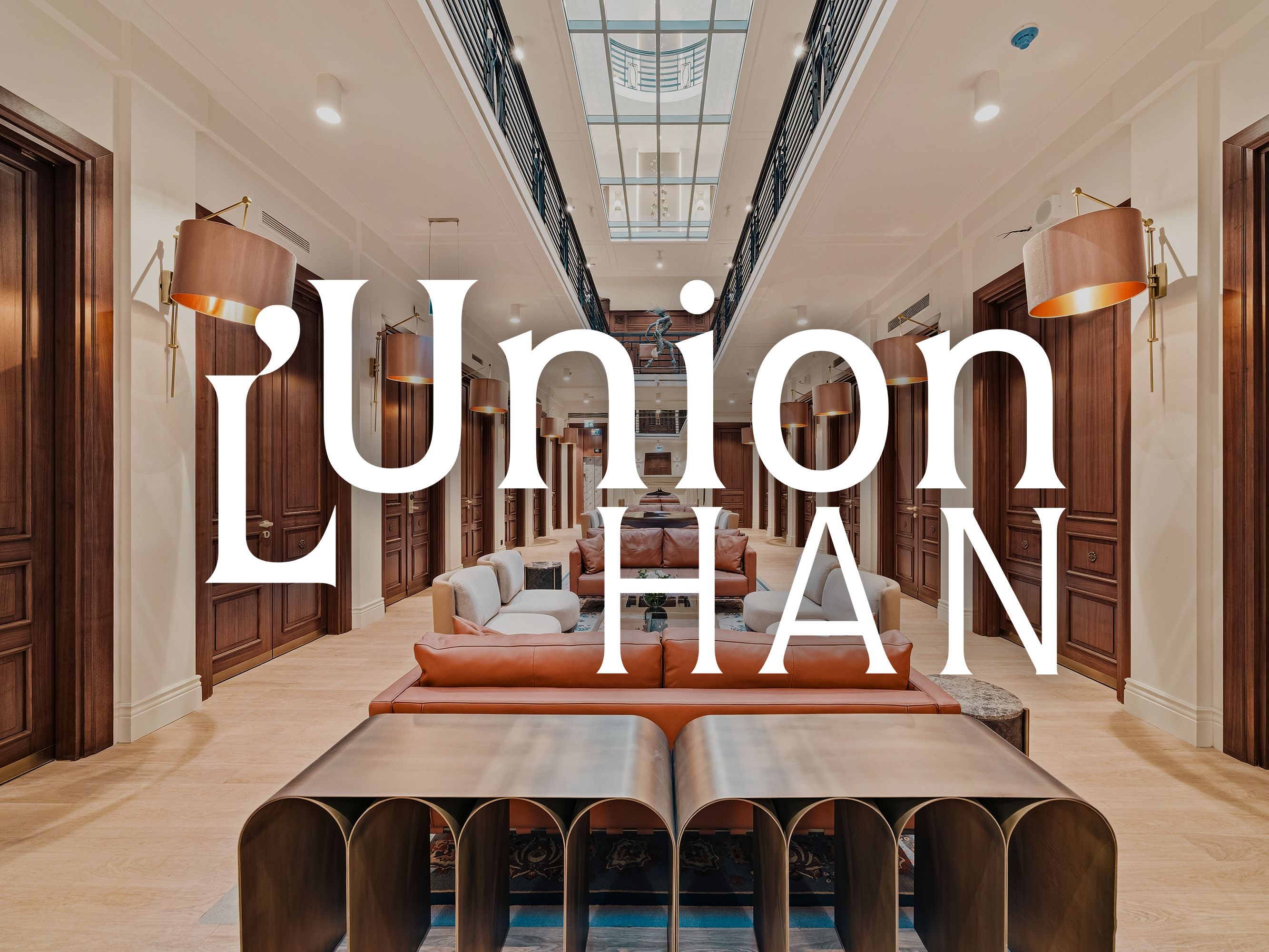 Hotel corridor with skylight, wood-paneled doors, and central seating area, overlaid with “L’Union Han” logo.