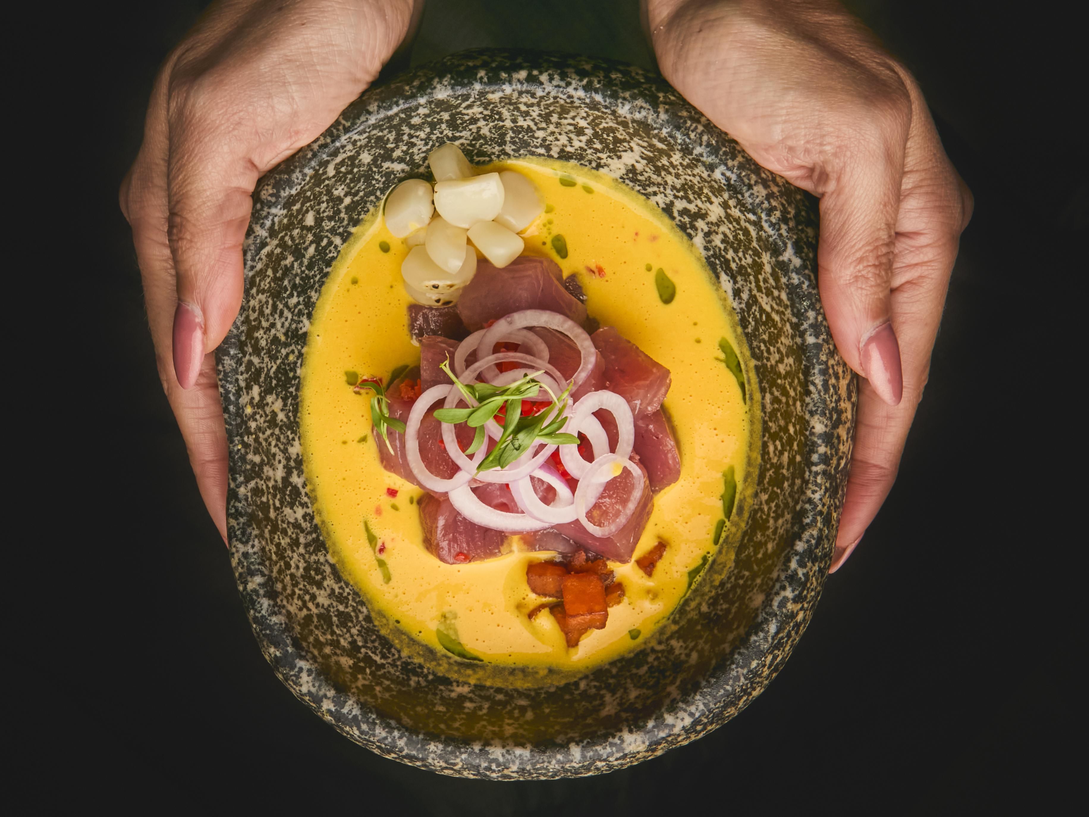 Waiter's hands offering a dish of fresh tuna with onions and garlic