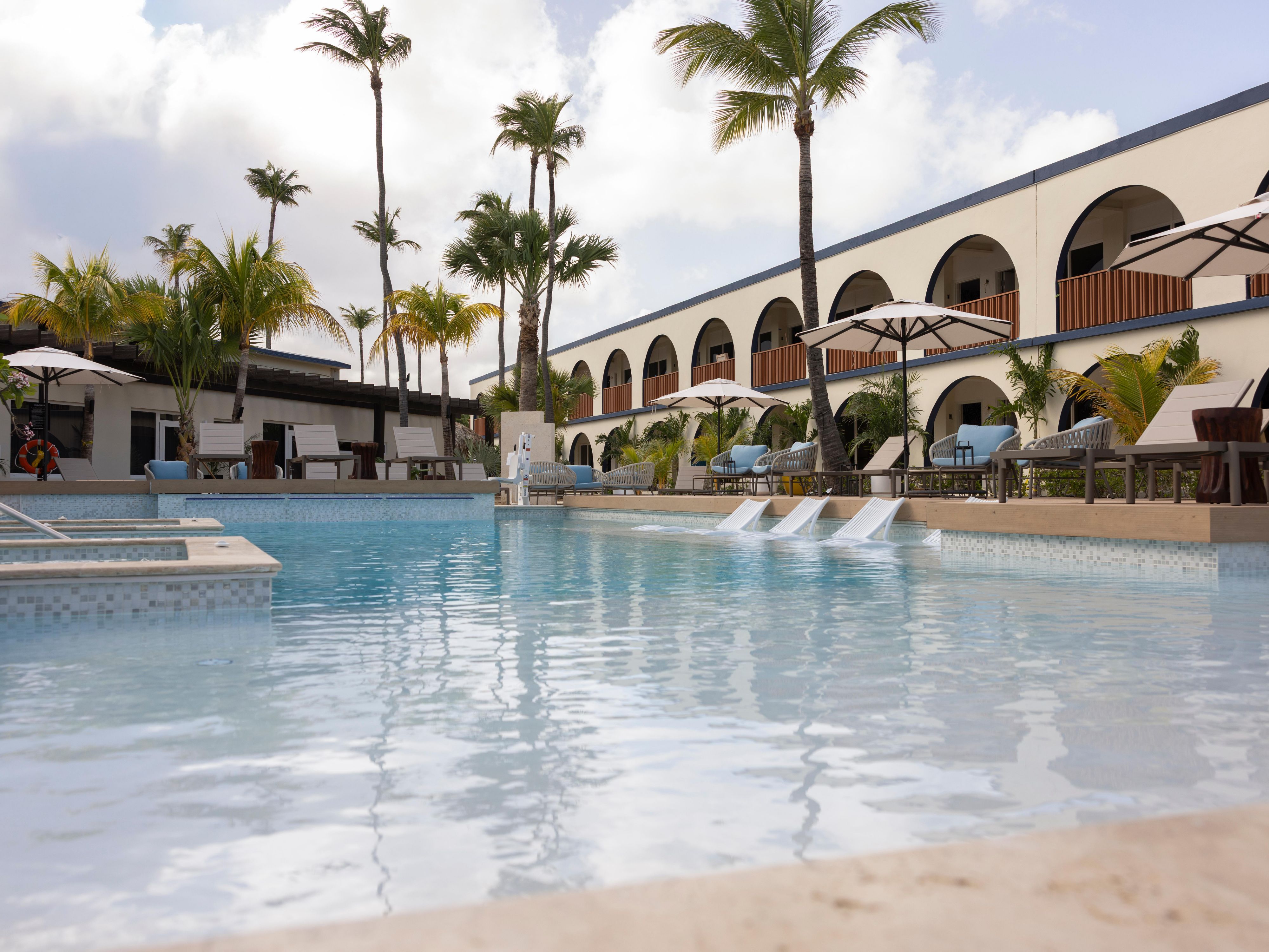 Relájese en nuestra paradisíaca piscina al aire libre. Dese un refrescante chapuzón en nuestra atractiva piscina, la manera perfecta de relajarse y refrescarse durante su estancia en nuestro hermoso hotel de Aruba. Tome el sol y disfrute del tranquilo ambiente isleño a solo unos pasos de su habitación.