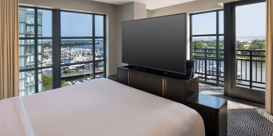 Compass Suite bedroom with pop-up TV console, balcony access, and expansive marina views.