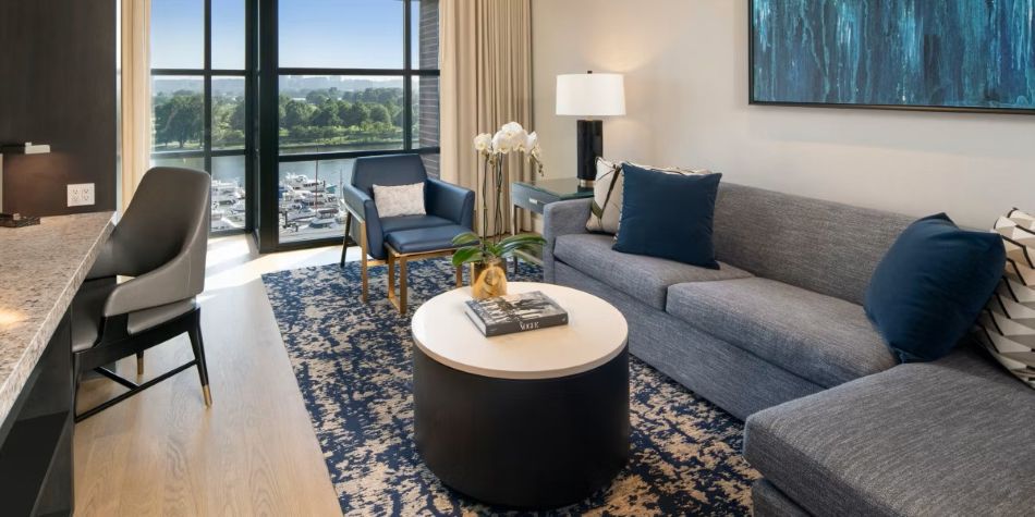 Compass Suite living area with grey sectional, blue accent chair, and marina views.