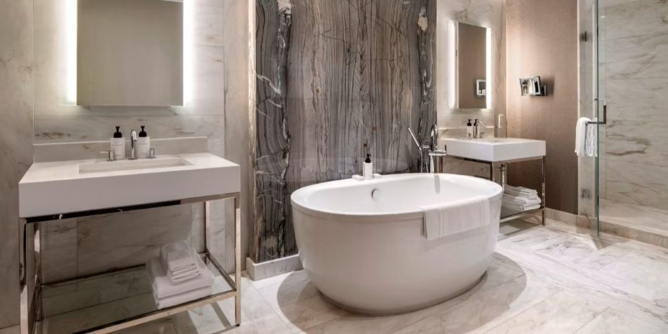 Constellation Suite bathroom with freestanding tub, dual vanities, glass shower, and marble walls.