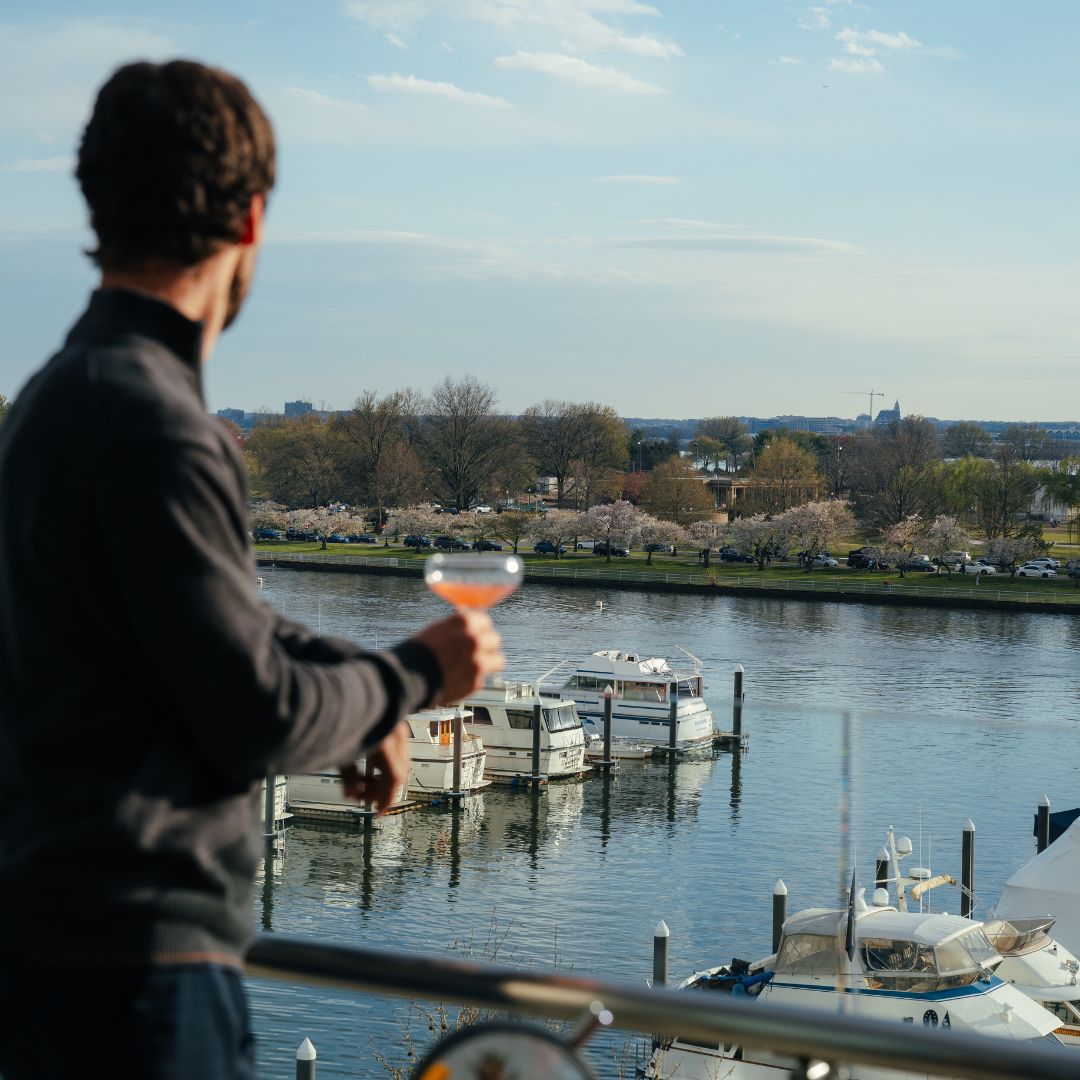 man on balcony overlooking harbor with cocktail in hand