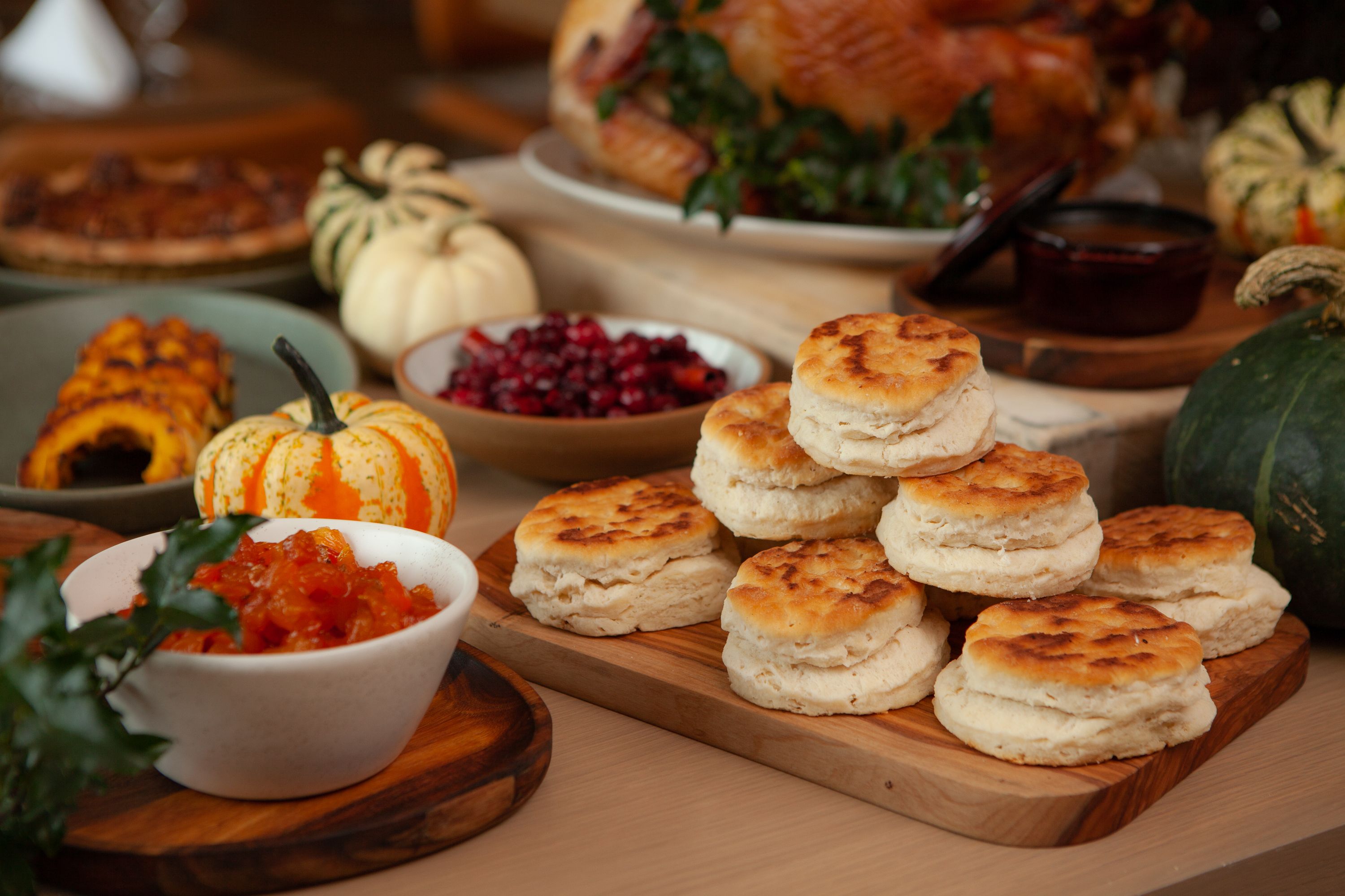 Thanksgiving spread with flaky biscuits, roasted turkey, cranberry relish, and seasonal pumpkins on a festive table.