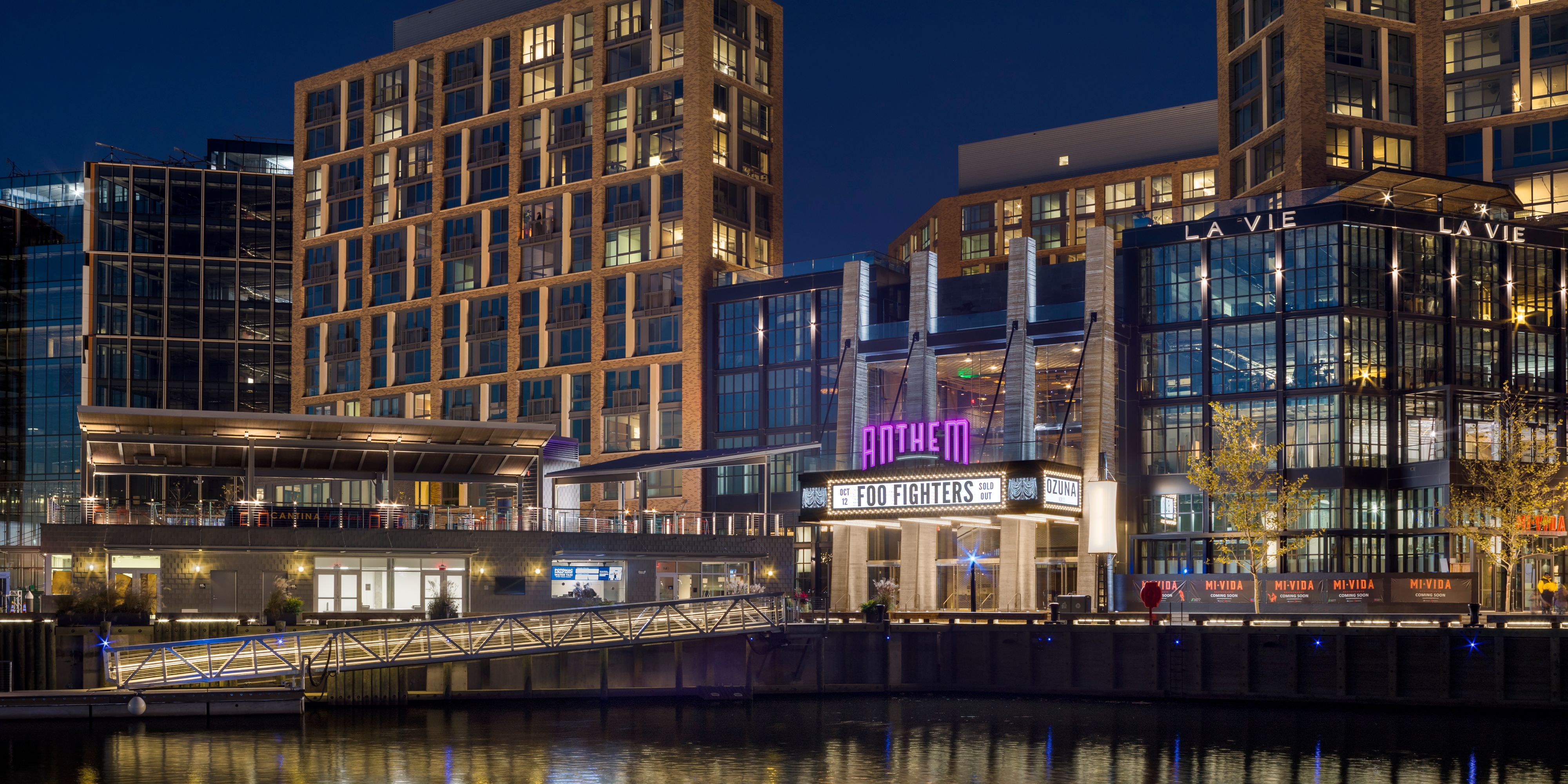 Exterior of The Anthem with a Foo Fighters sign lit up, shown from across the water at night.
