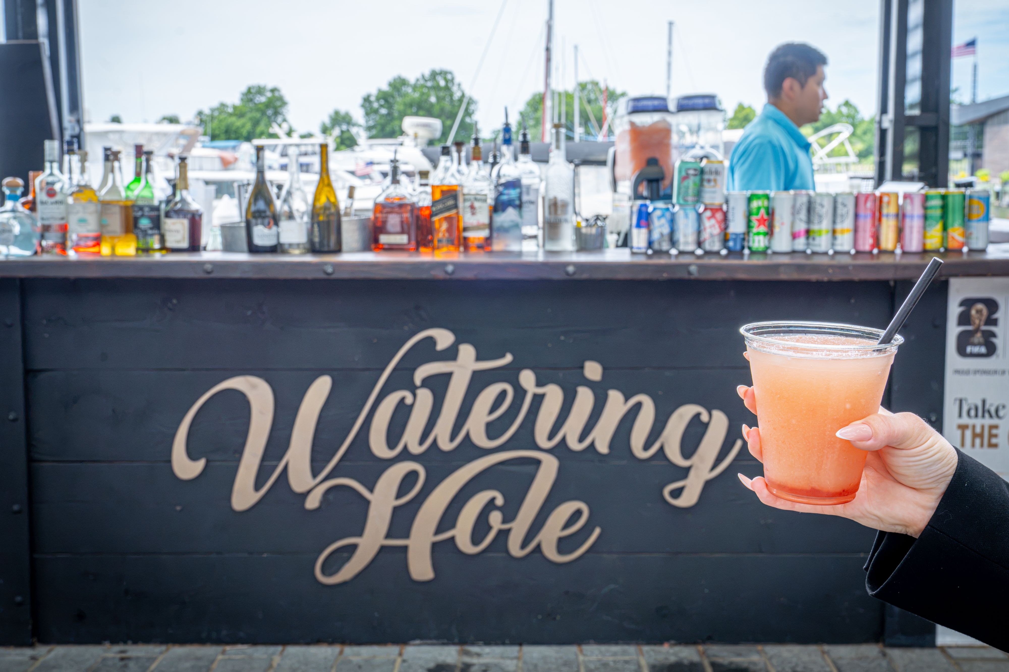 and holding a pink frozen cocktail at The Watering Hole outdoor bar, with bottles lined along the counter in Washington, D.C.