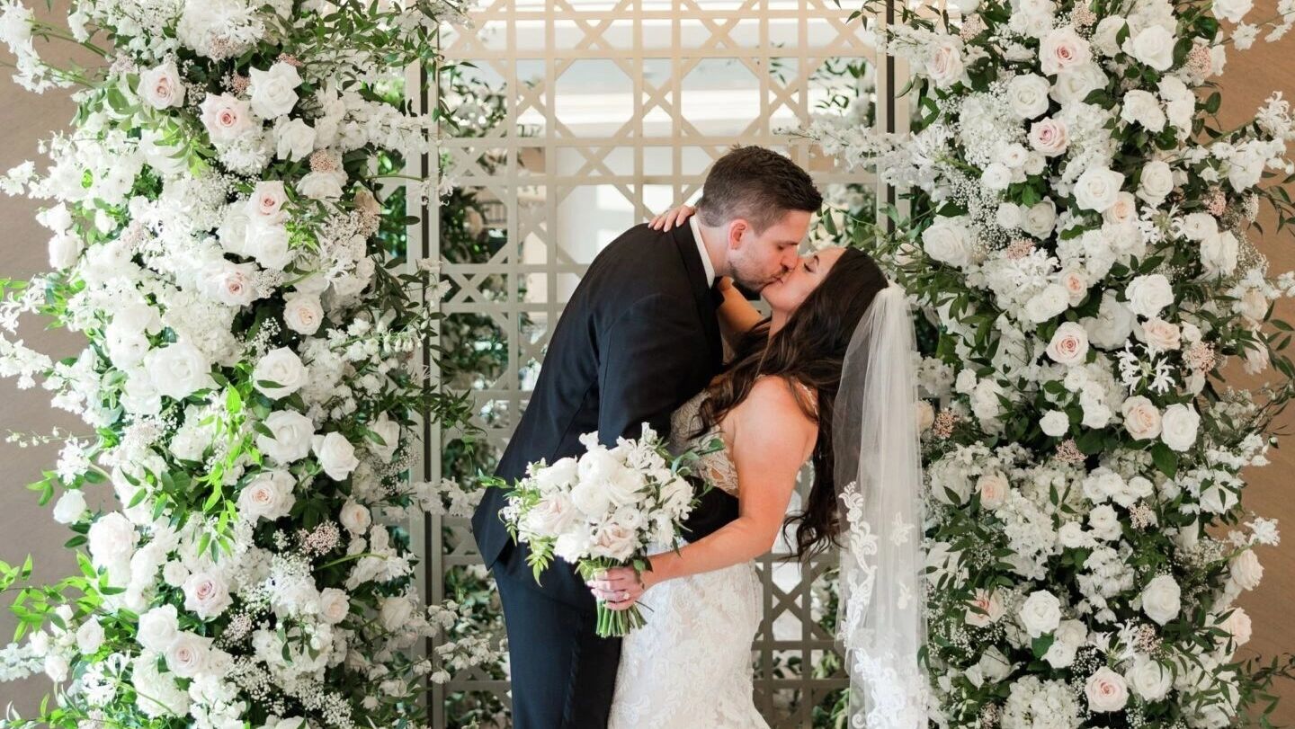 bride and groom kissing in front of flower arch