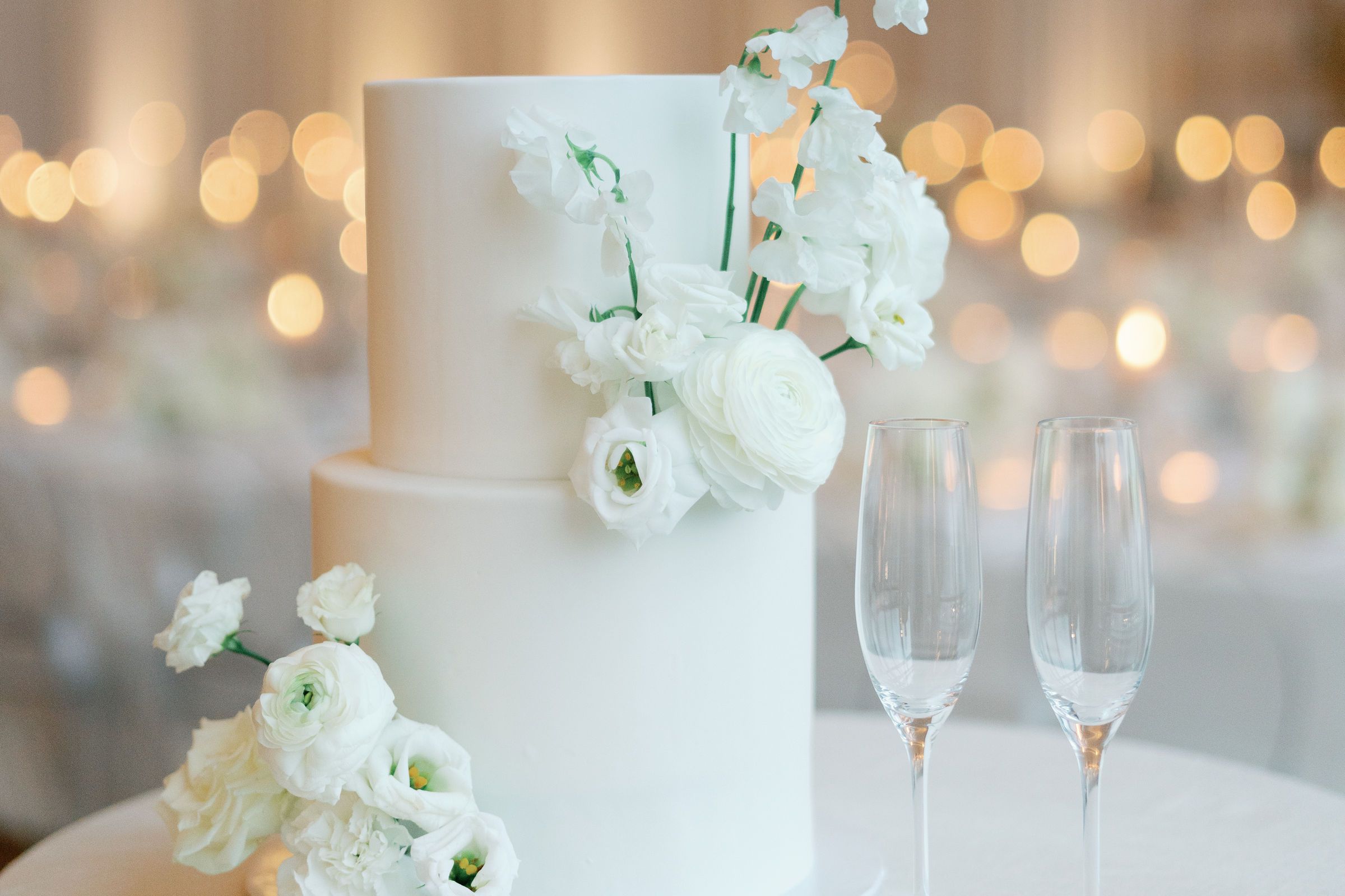 Two-tier white wedding cake with champagne flutes and flowers