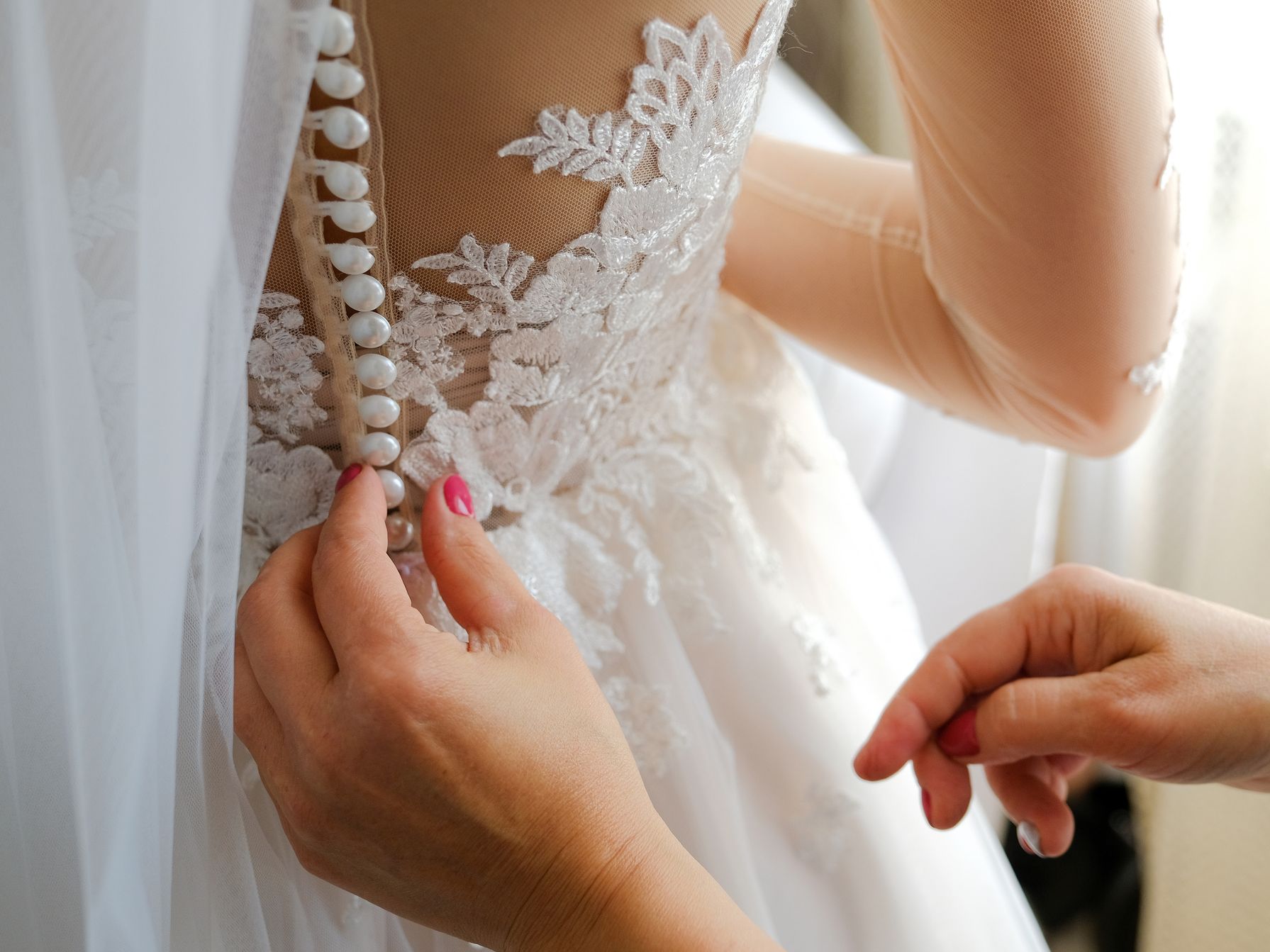 Hands fastening the lace back of a wedding dress.