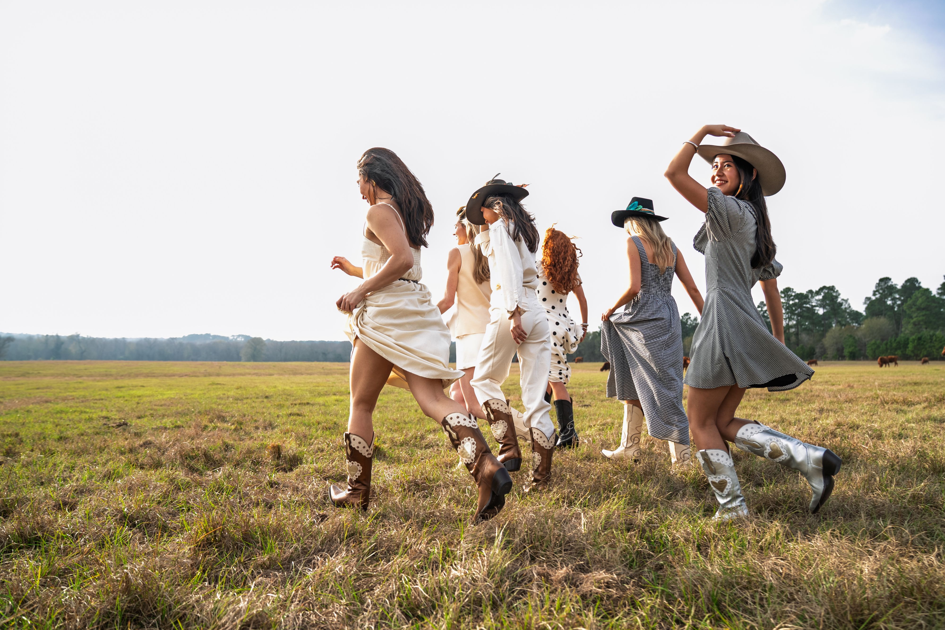 Group of women in dresses and cowboy boots walking together through an open field.