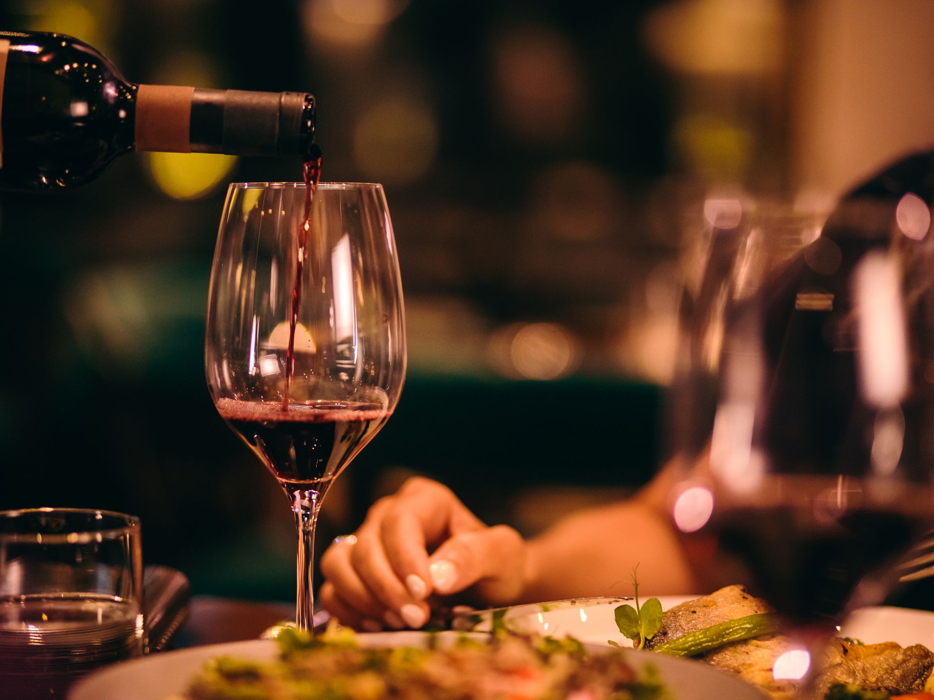 Server pouring wine into guest's glass at dinner.