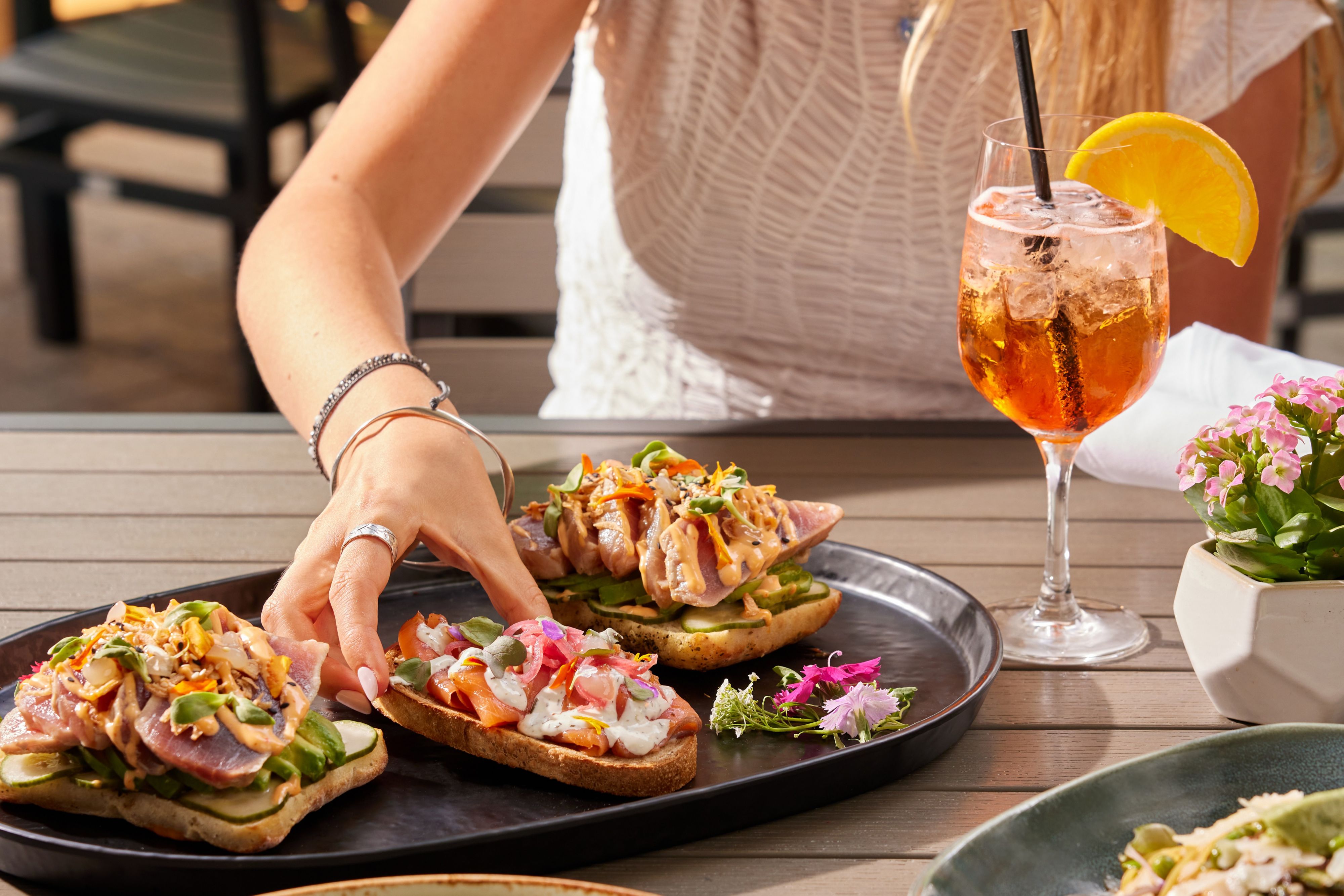 Open-faced seafood toasts with cocktail on outdoor dining table.