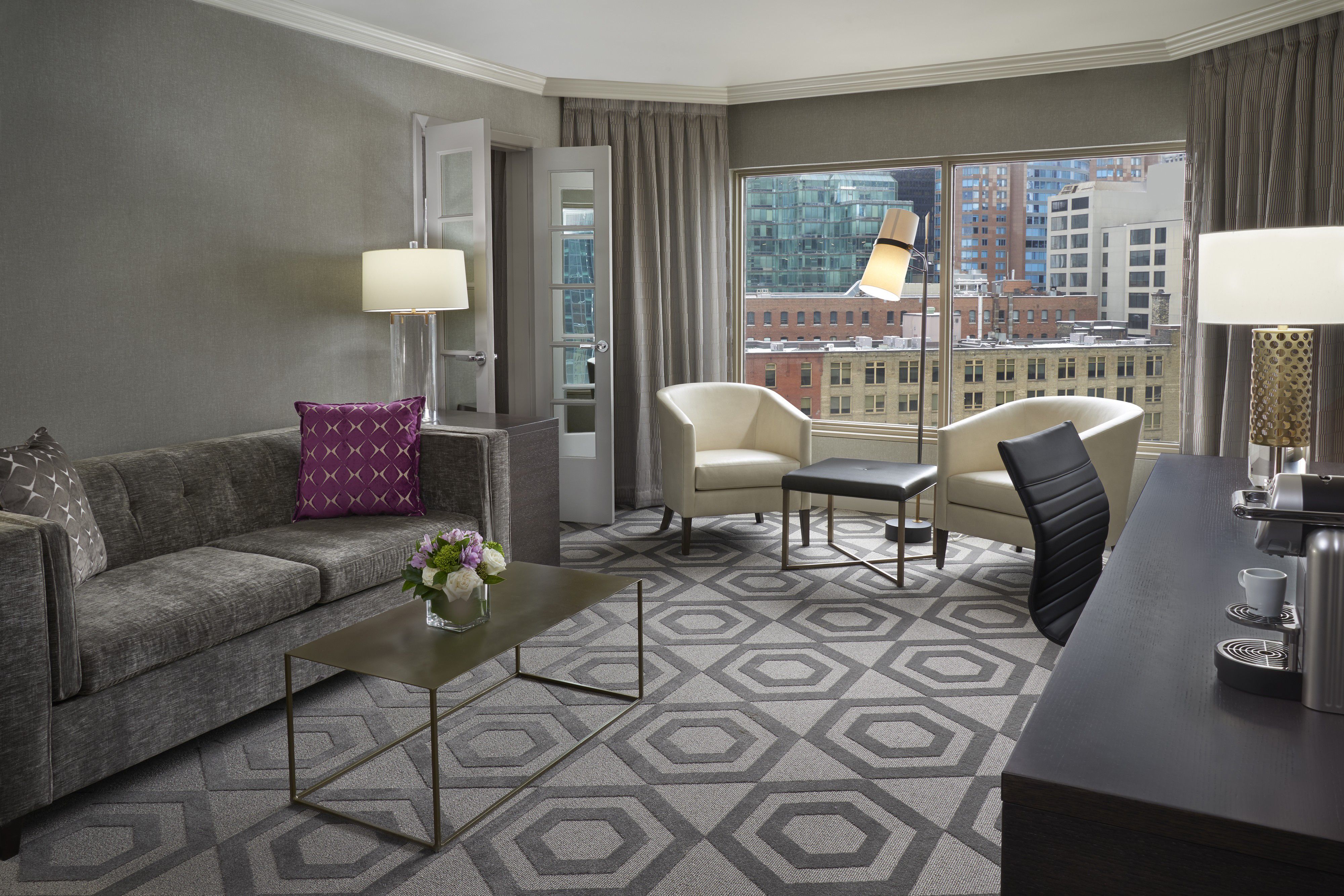 Spacious suite living area with sofa, lounge chairs, and city views