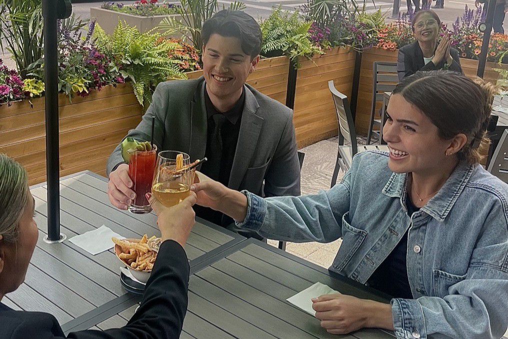 Guests clink cocktails at a casual outdoor dining setting.