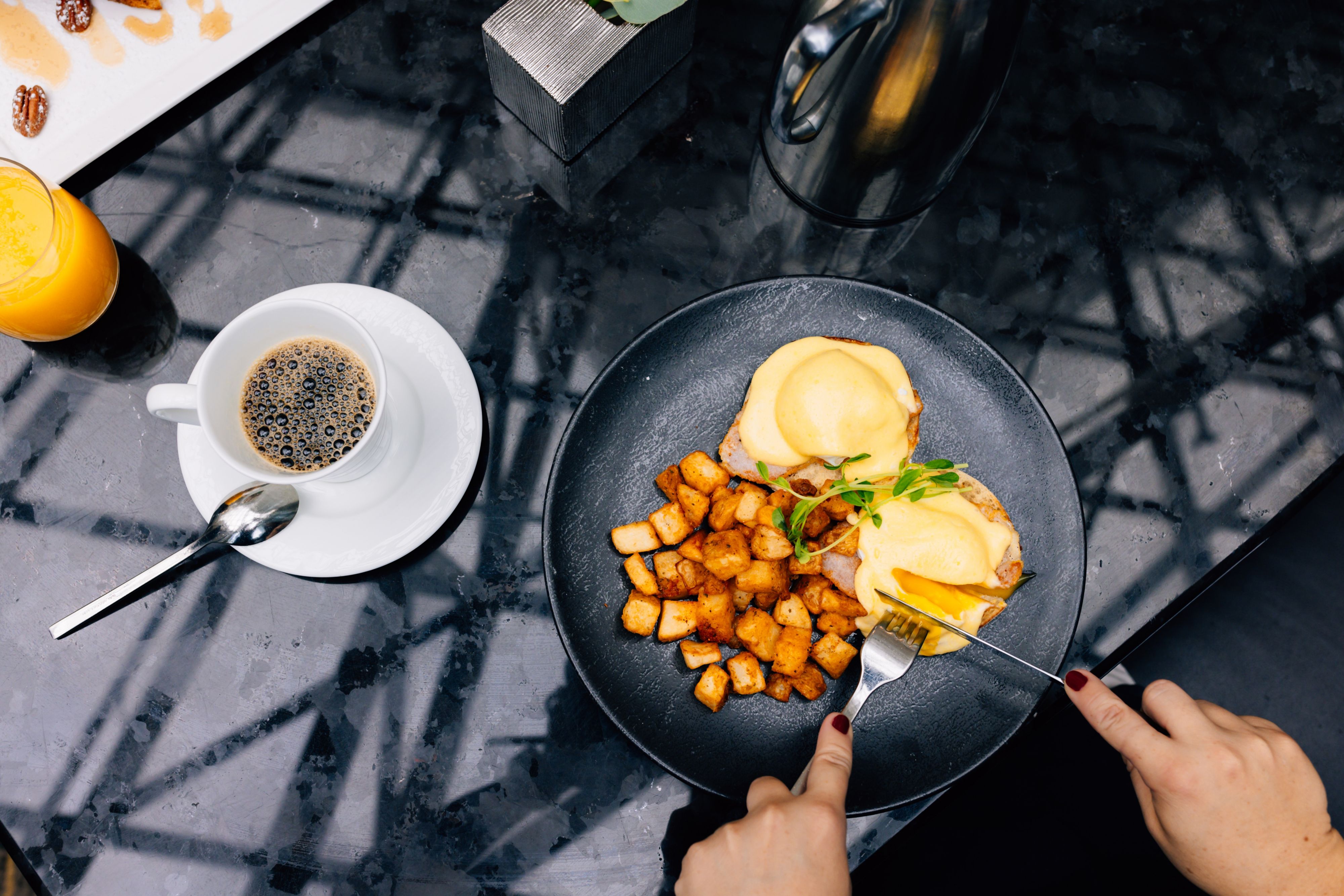 Eggs benedict dish witg roasted potatos and a cup of coffee